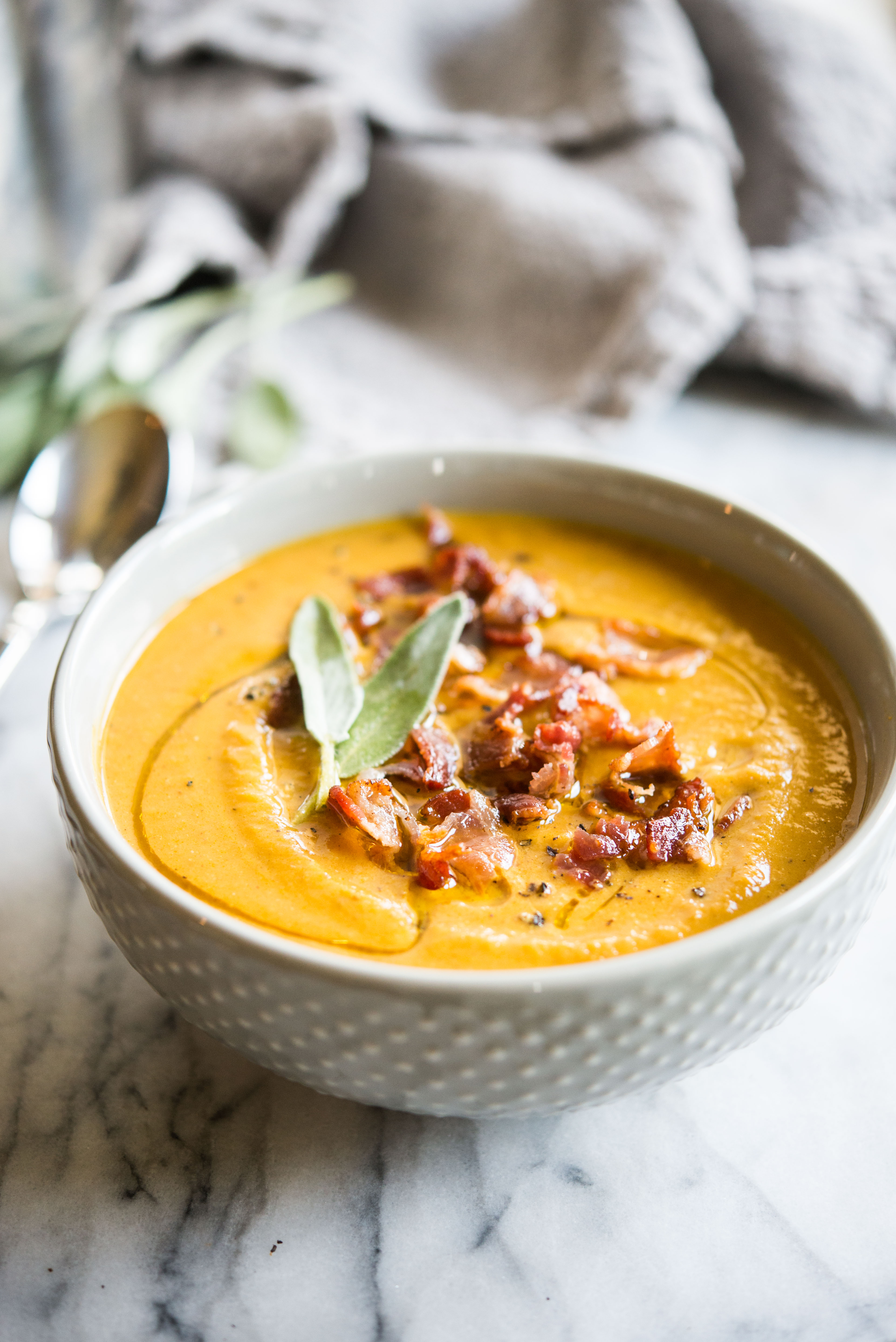 Instant pot pumpkin soup in a grey bowl topped with bacon and sage on a marble board