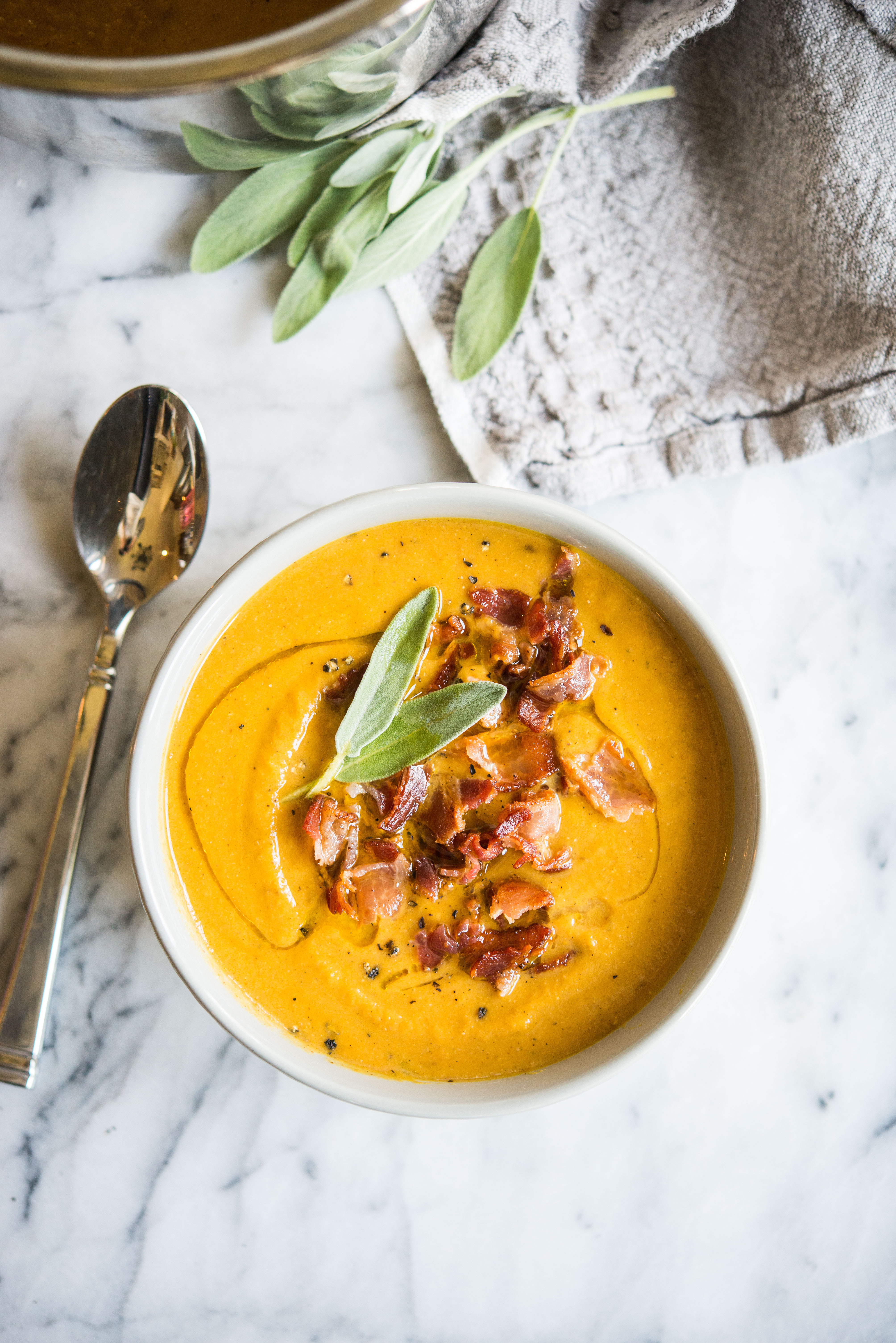 pumpkin soup topped with bacon and sage in a grey bowl on a marble board 