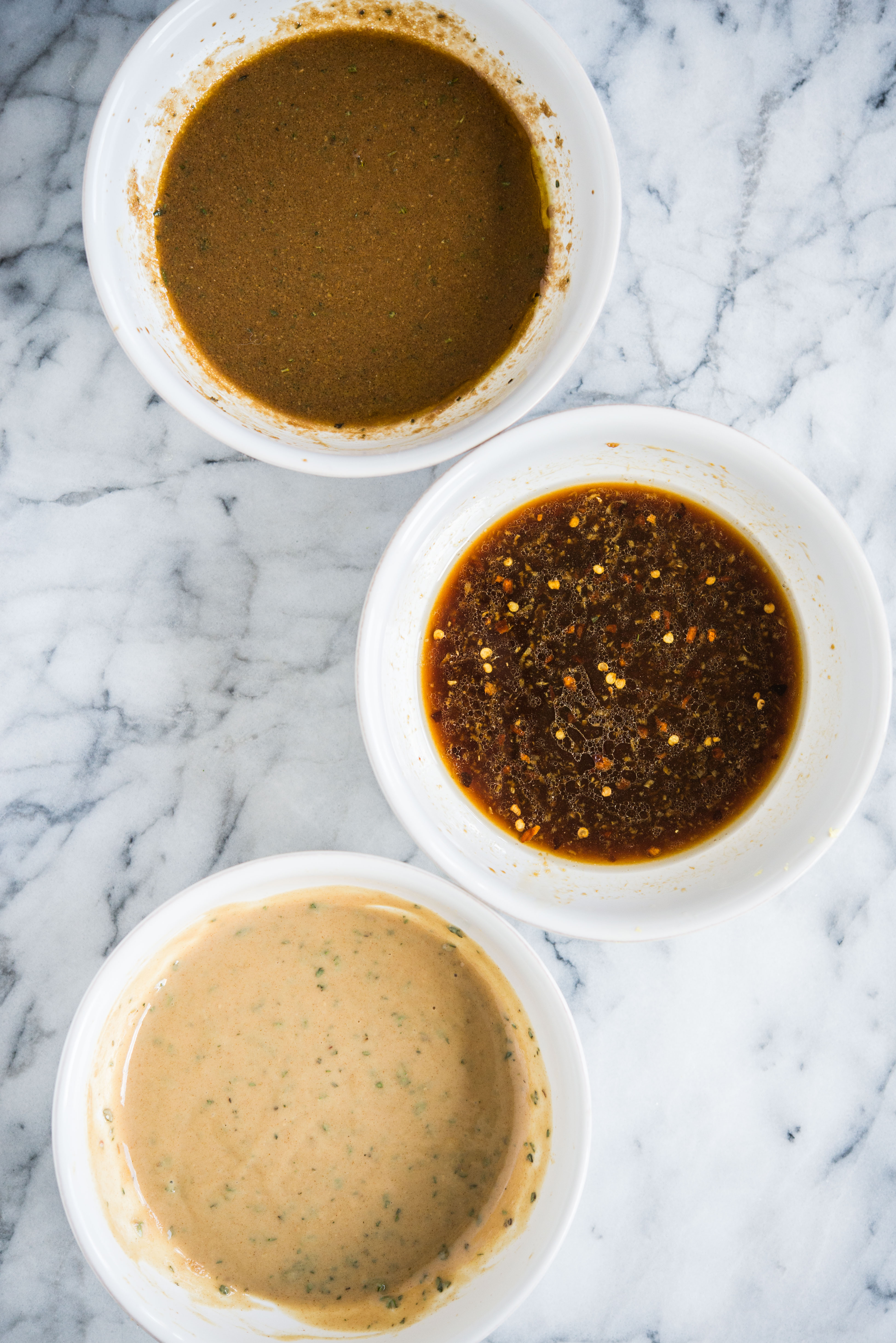 3 pork tenderloin marinades - sesame ginger, maple dijon, and balsamic rosemary in white bowls on a marble countertop