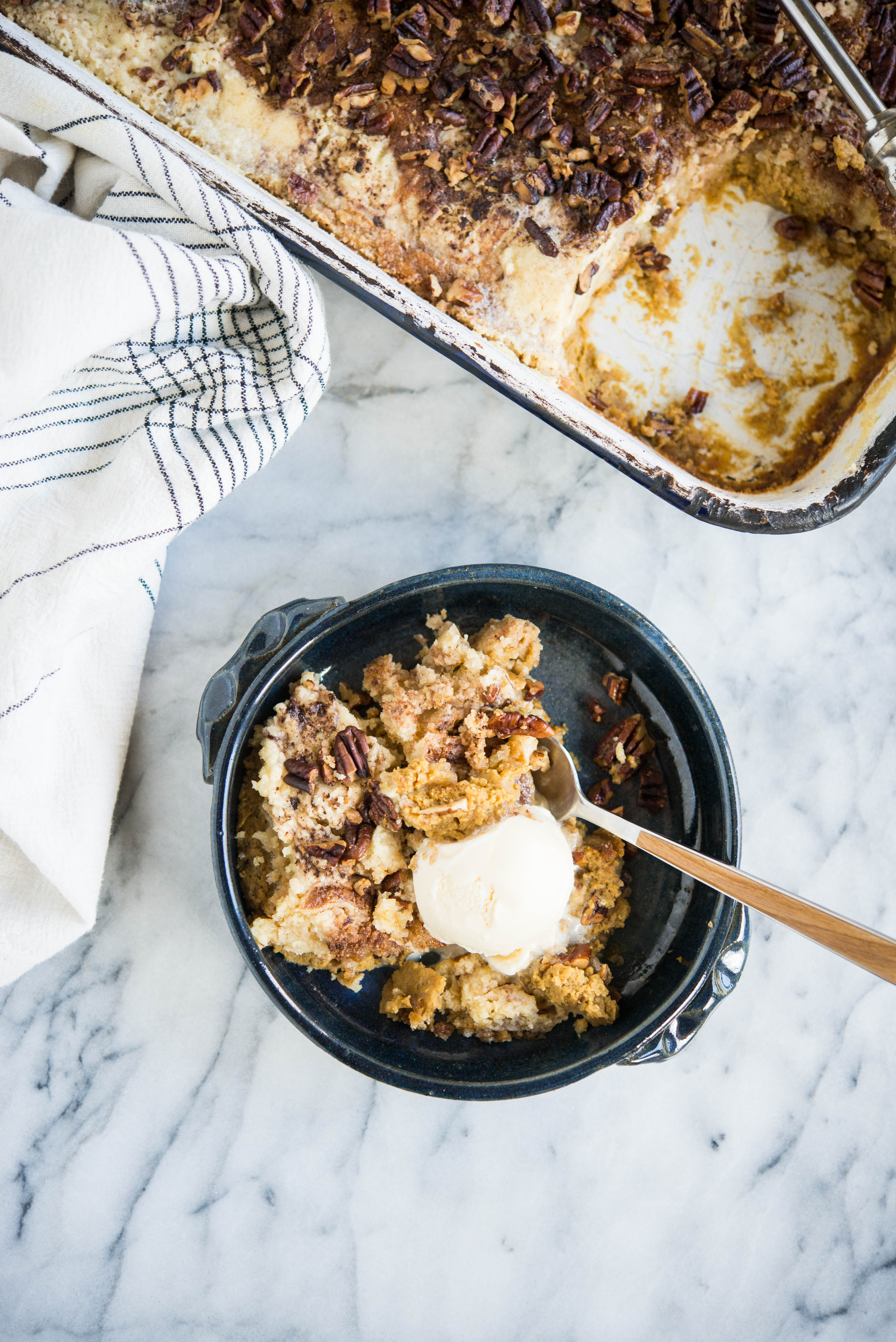 pumpkin pie dump cake in a dark blue bowl with a scoop of ice cream on top