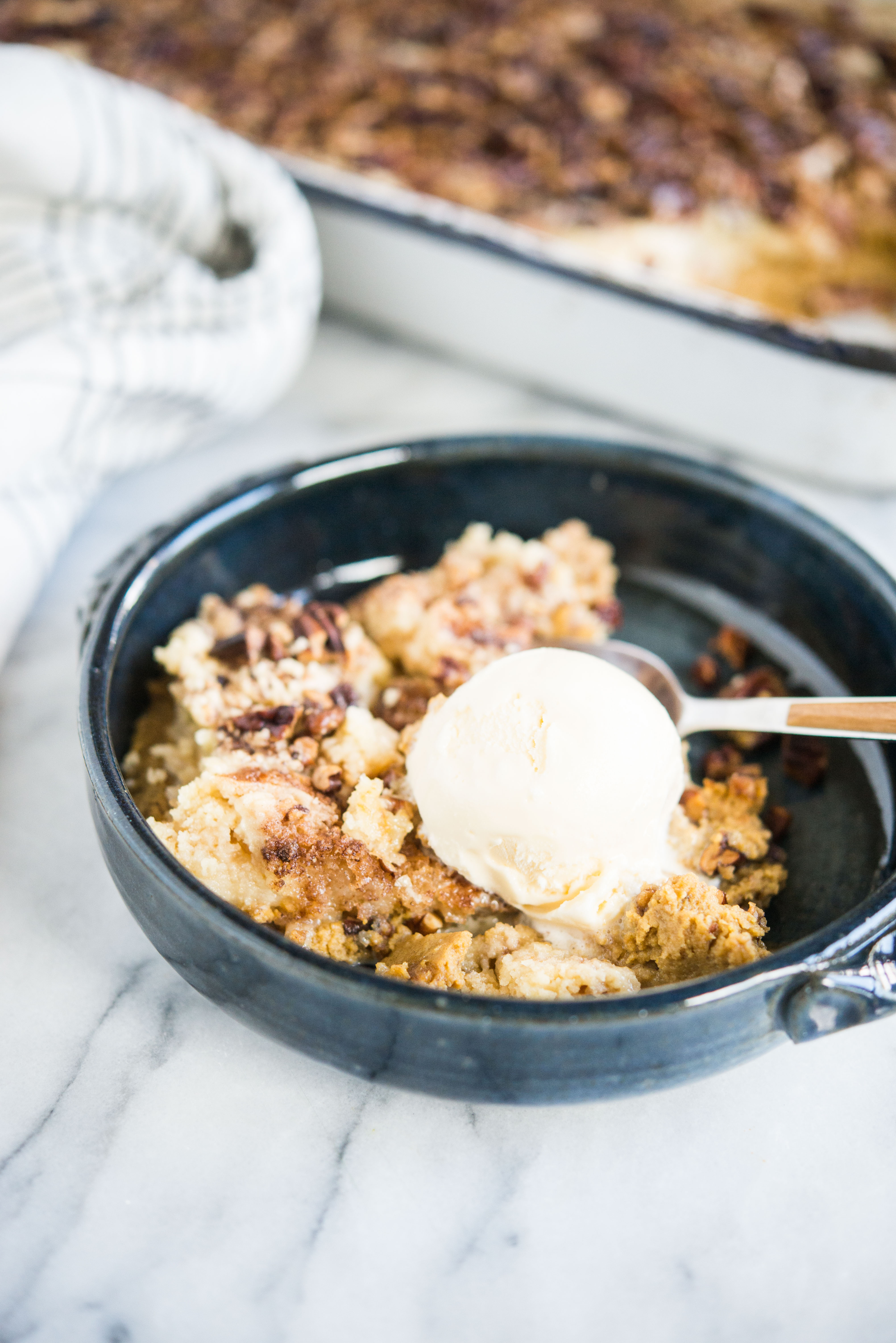 pumpkin pie dump cake in a dark blue bowl with a scoop of ice cream on top