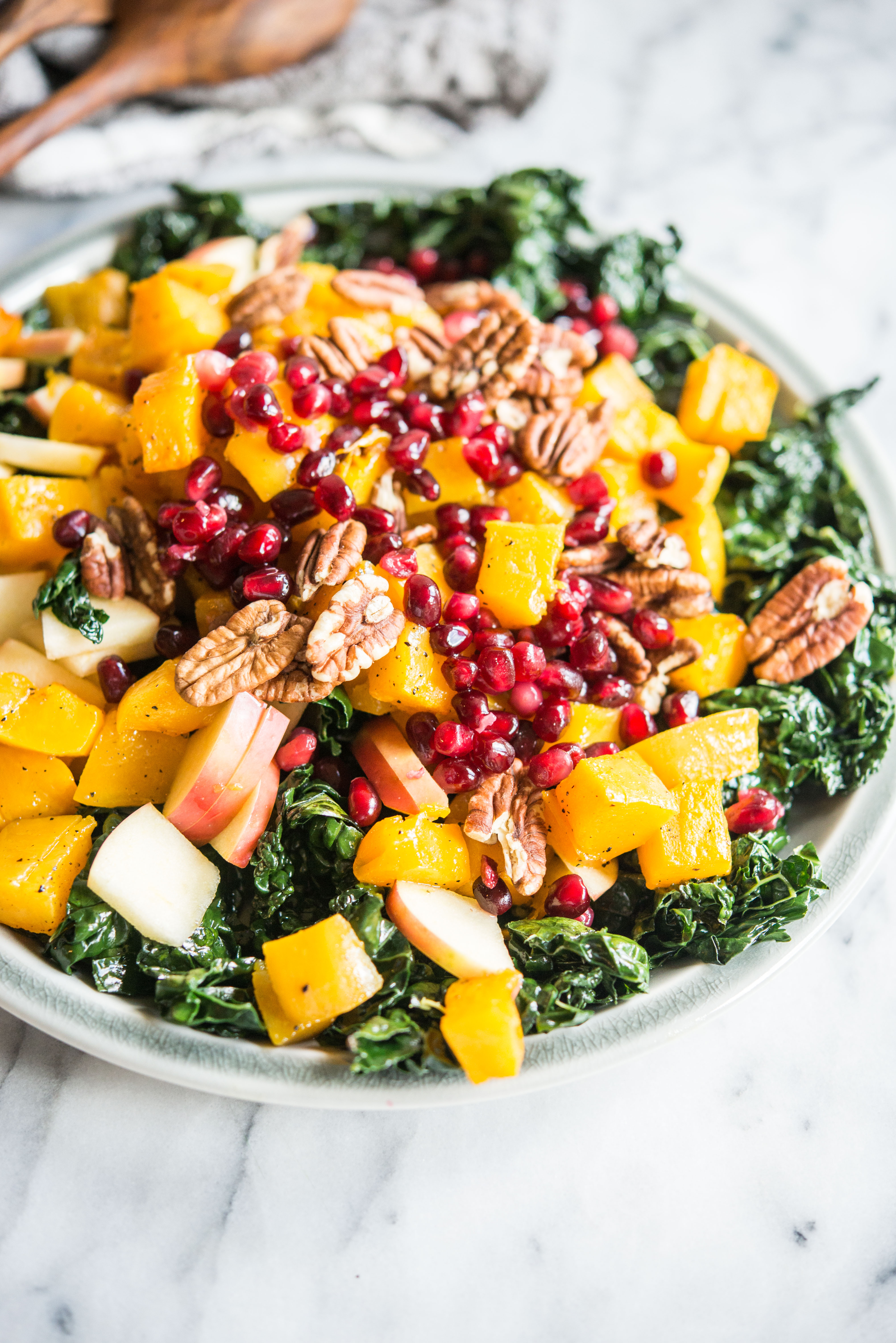 kale salad with roasted butternut squash, pecans, apples, and pomegranate seeds on a gray plate on a marble board