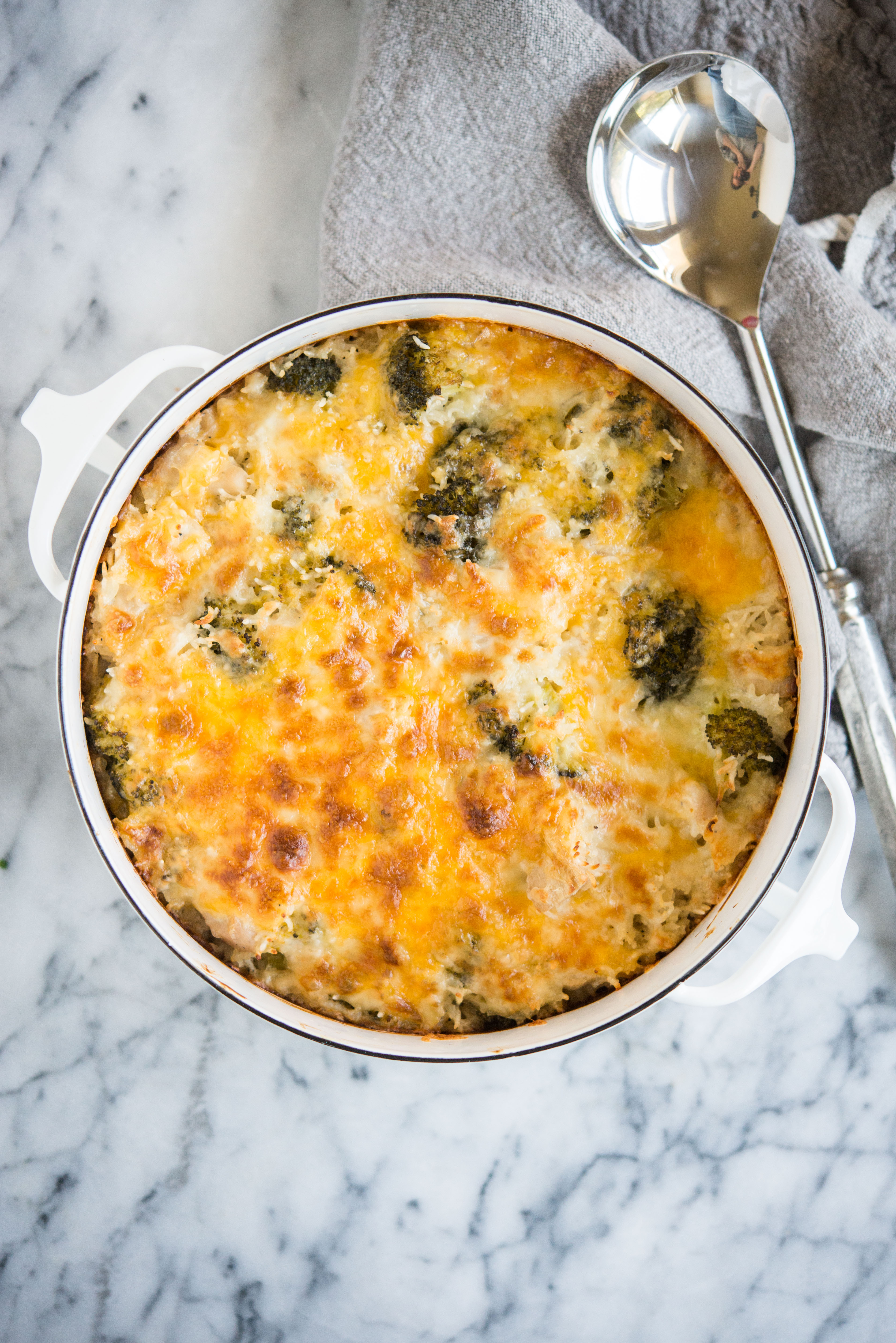 chicken broccoli and rice casserole with cheese in a white casserole dish on a marble surface