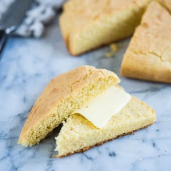 a wedge of gluten-free cornbread cut in half with a slice of butter in the middle on a marble surface