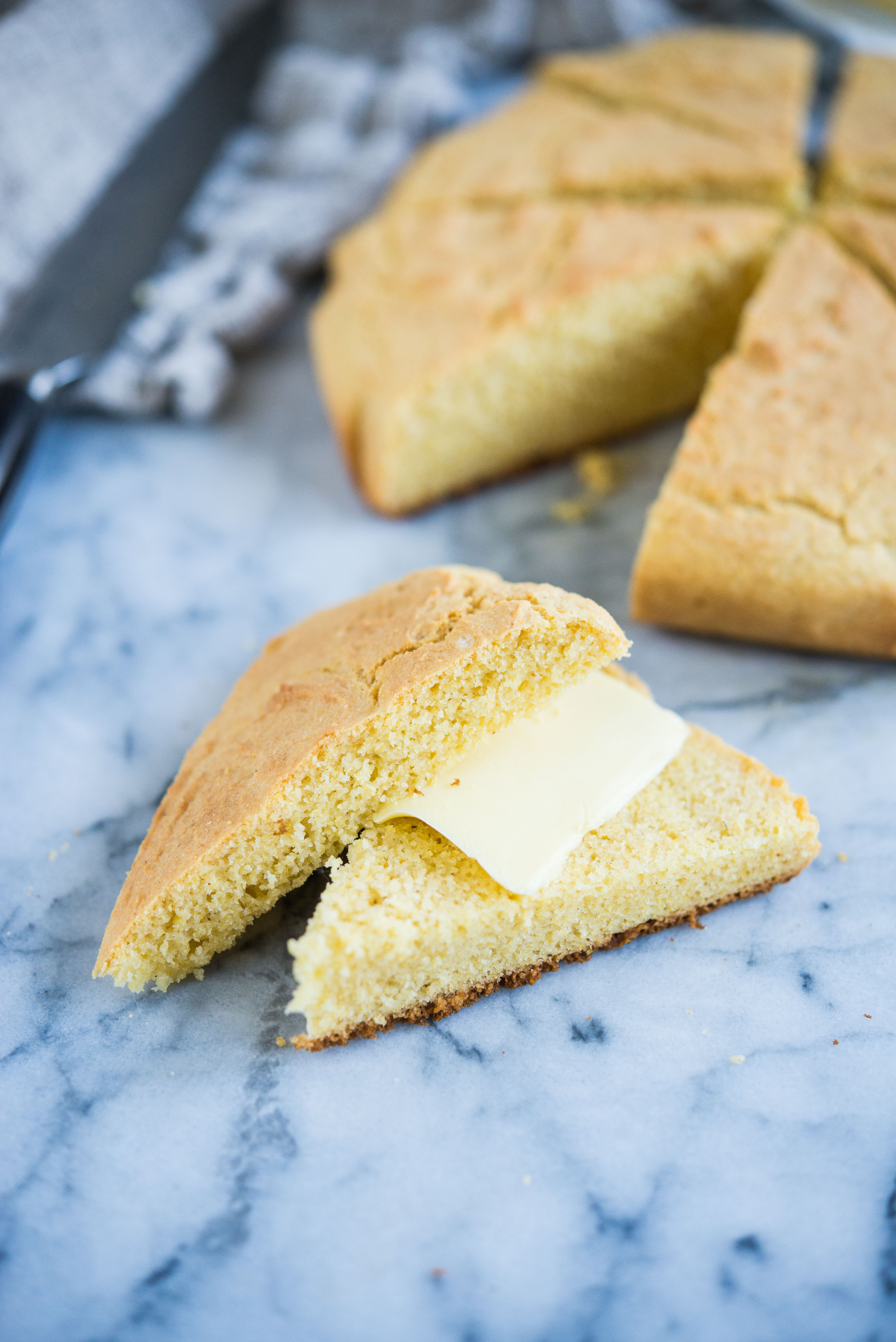 a wedge of gluten-free cornbread cut in half with a slice of butter in the middle on a marble surface