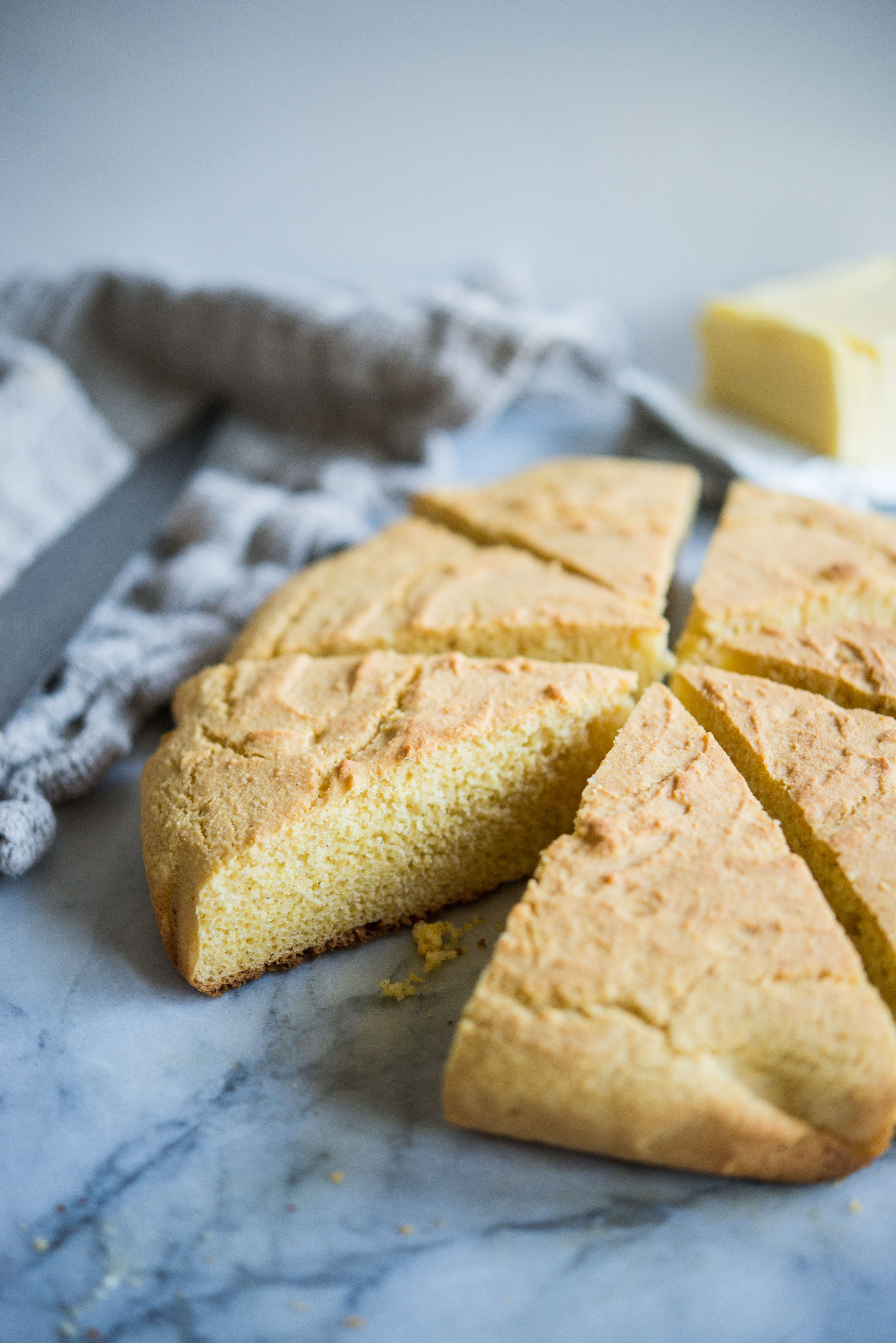 a round loaf of gluten-free cornbread cut into 6 wedges on a marble countertop with a grey towel in the background