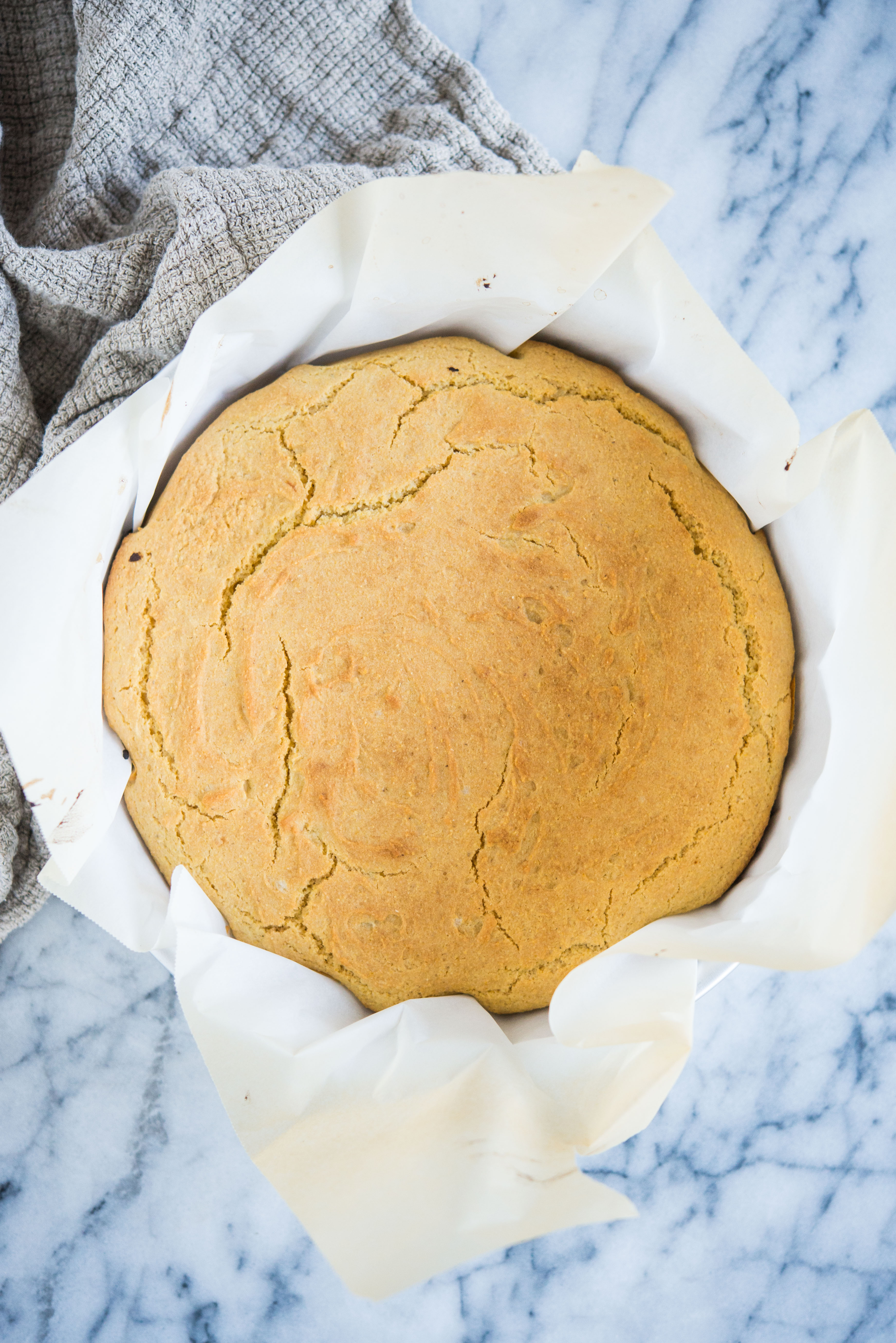 gluten free cornbread in a round cake pan lined with parchment paper on a marble surface