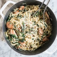 one pot pasta with Italian sausage, kale, and parmesan cheese in a white cast iron pot on a marble surface