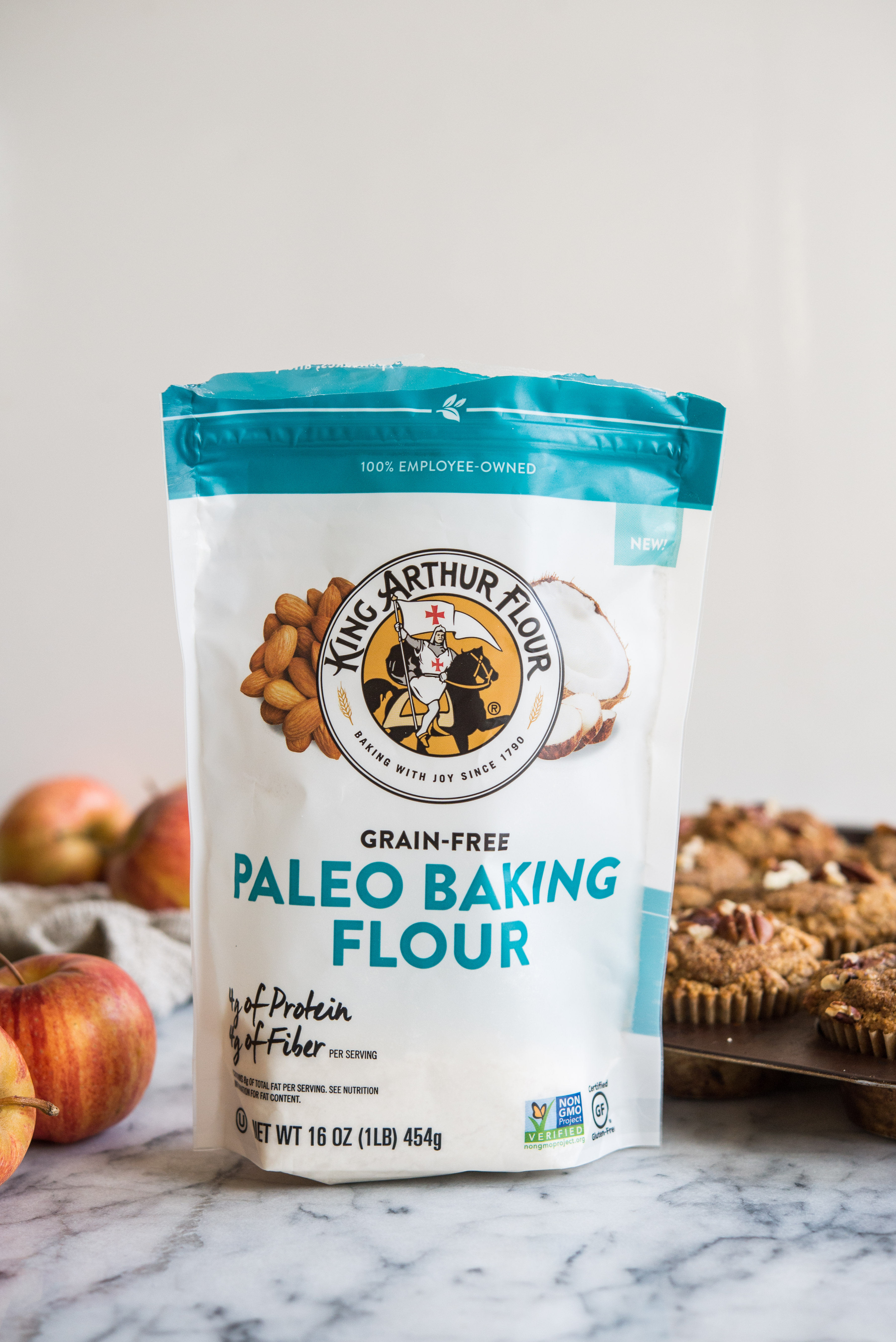 a bag of king arthur paleo baking flour on a marble board with muffins and apples in the background