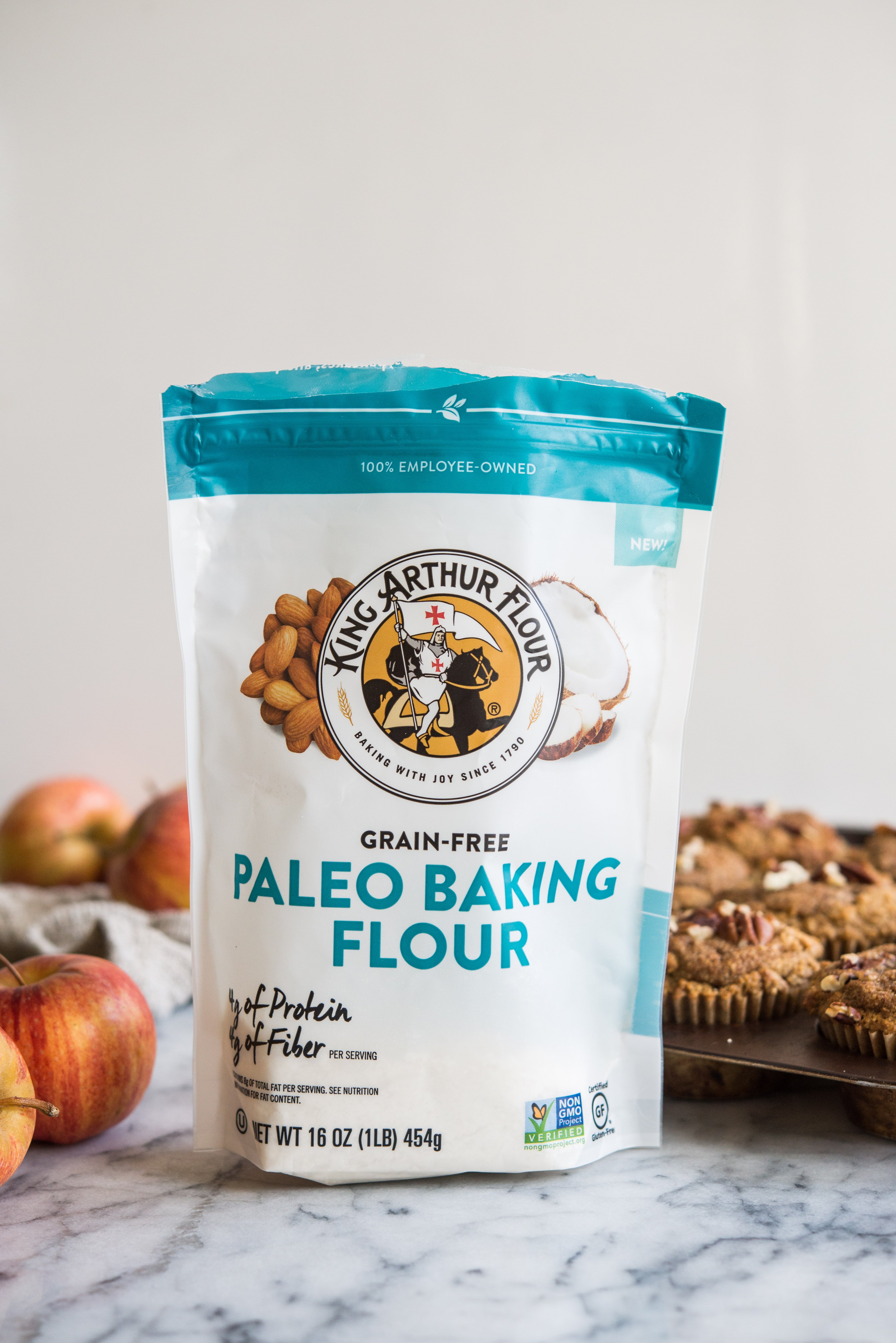 a bag of king arthur paleo baking flour on a marble board with muffins and apples in the background