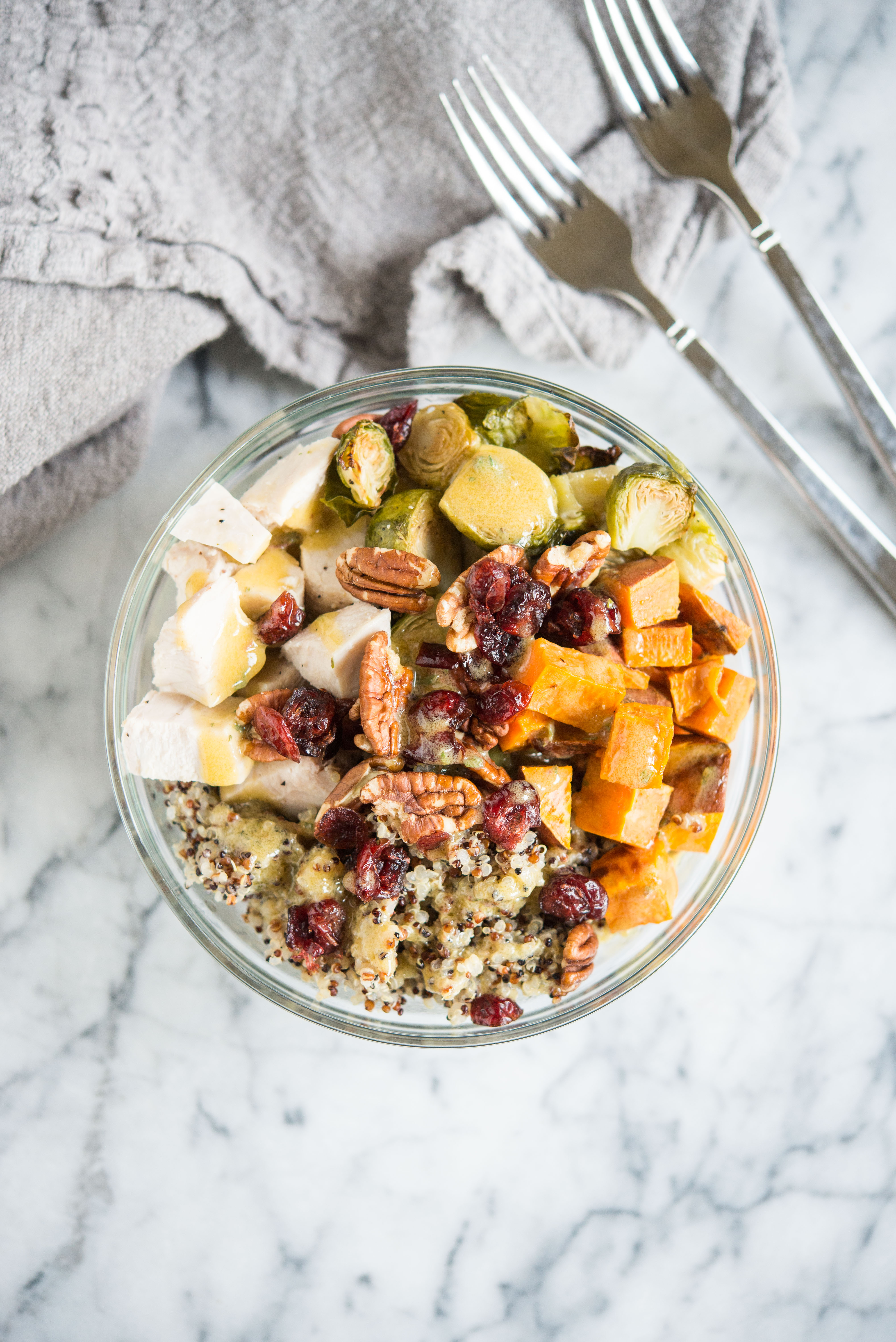 quinoa bowls with sweet potatoes, chicken, brussels spouts, pecans, and cranberries in a glass bowl on a marble countertop