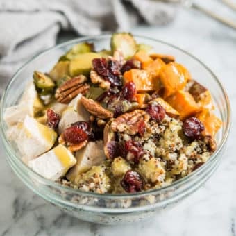 quinoa bowls with sweet potatoes, chicken, brussels spouts, pecans, and cranberries in a glass bowl on a marble countertop
