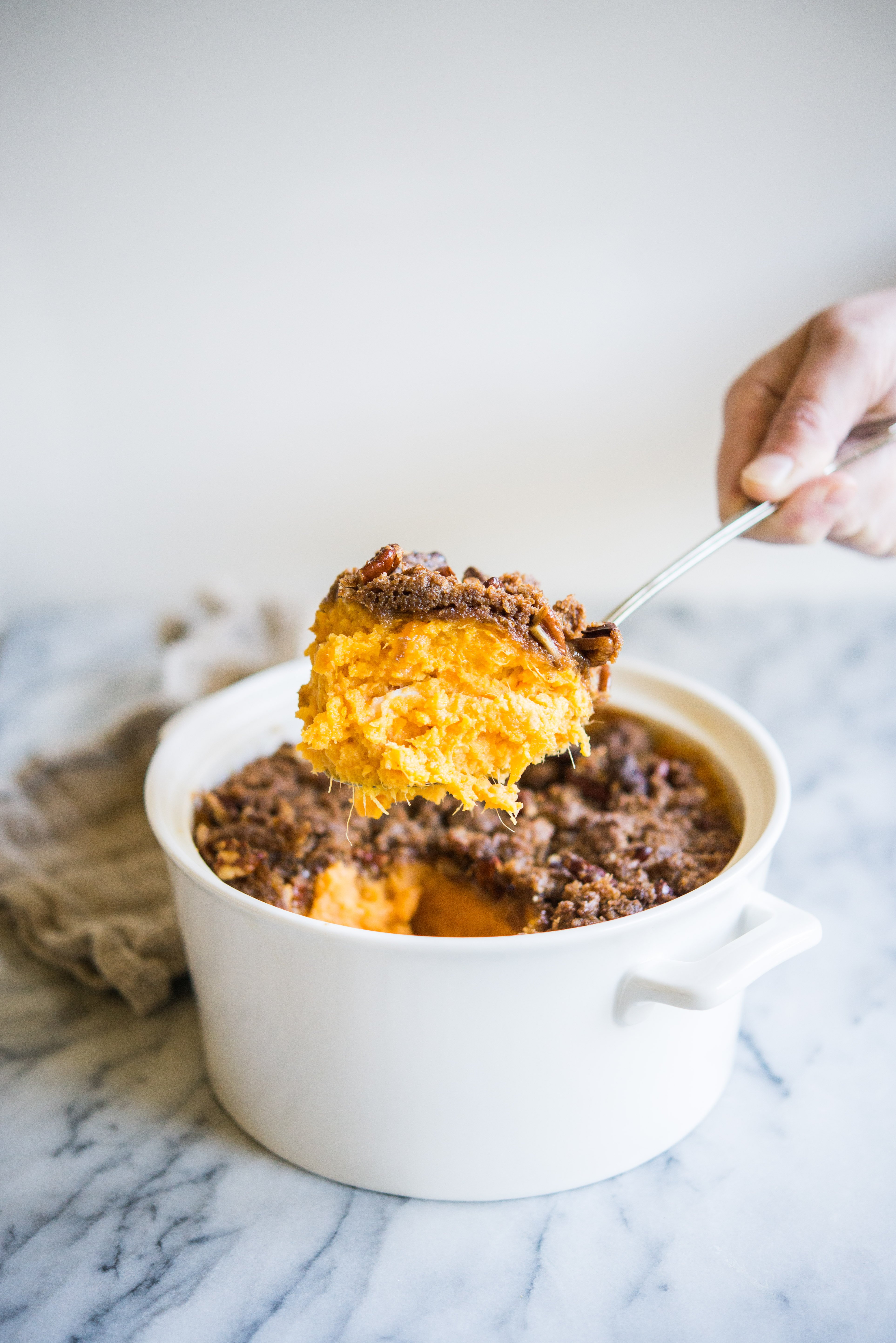 sweet potato casserole with pecans being scooped out of a white casserole dish