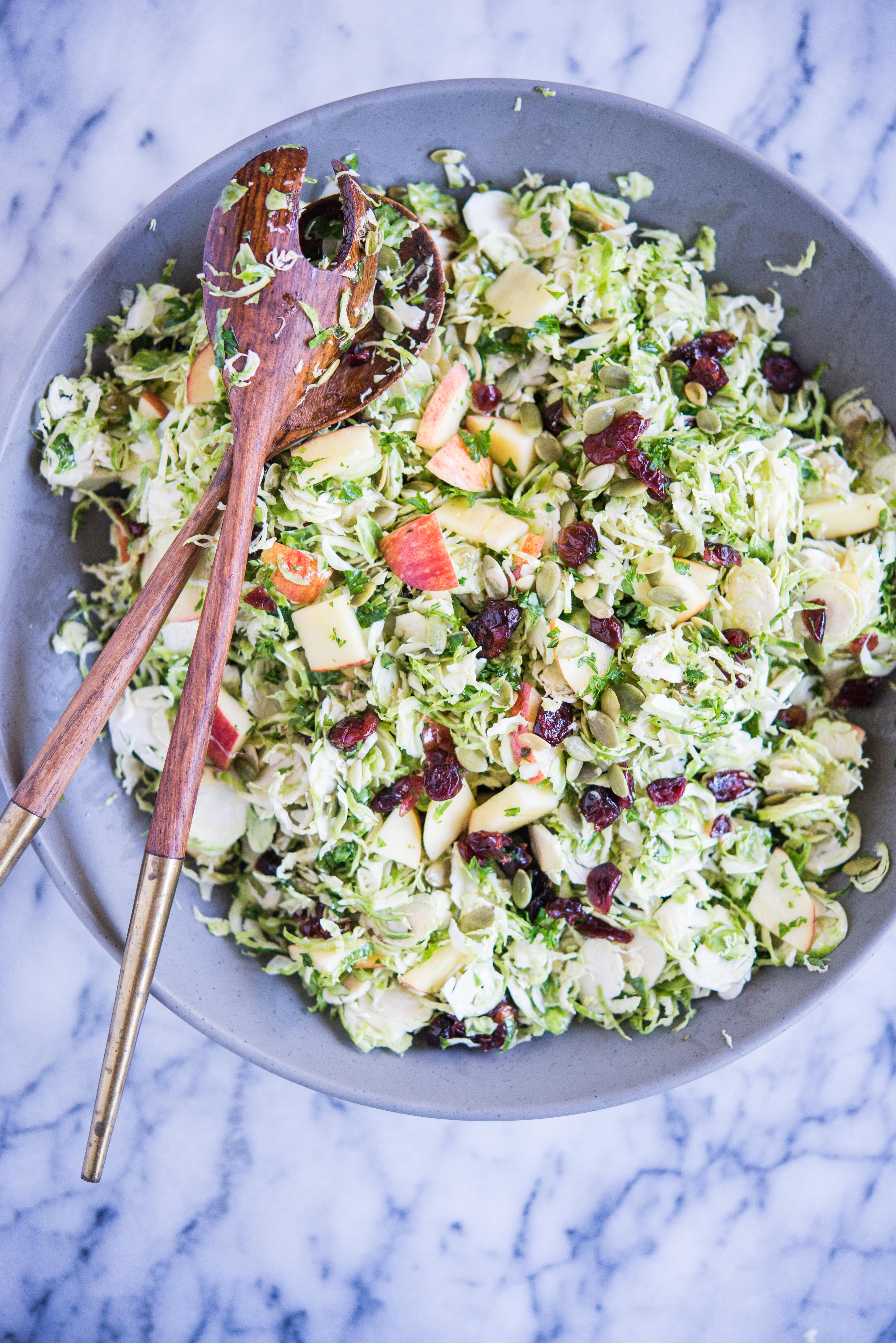 shaved brussels sprouts salad with apples, cranberries, and pumpkin seeds in a large gray bowl on a marble surface