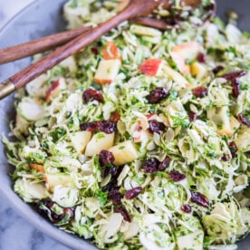shaved brussels sprouts salad with apples, cranberries, and pumpkin seeds in a large gray bowl on a marble surface