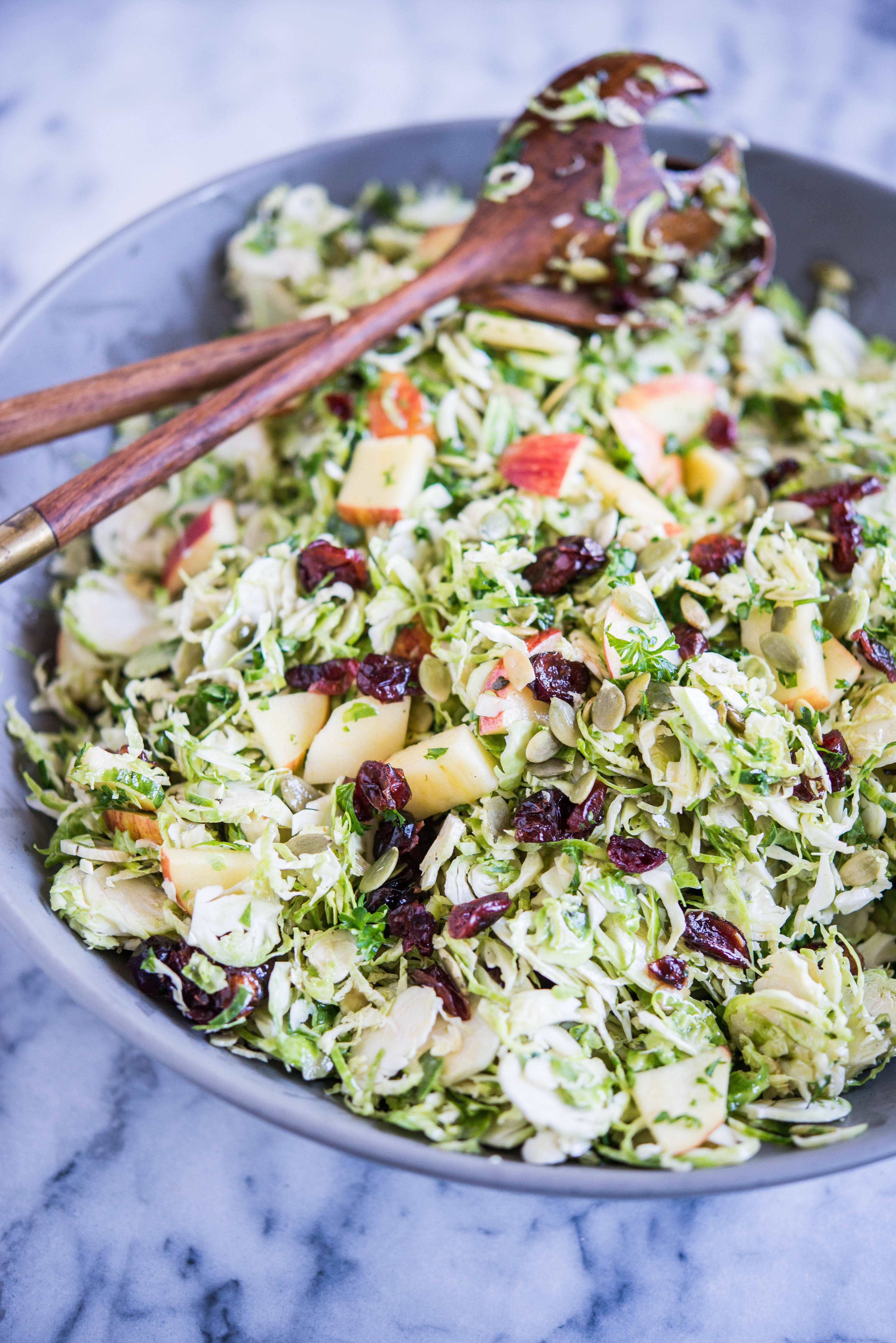 shaved brussels sprouts salad with apples and cranberries in a grey bowl on a marble surface