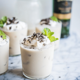 clear glasses filled with vegan baileys and topped with whipped cream, shaved chocolate, and mint leaves