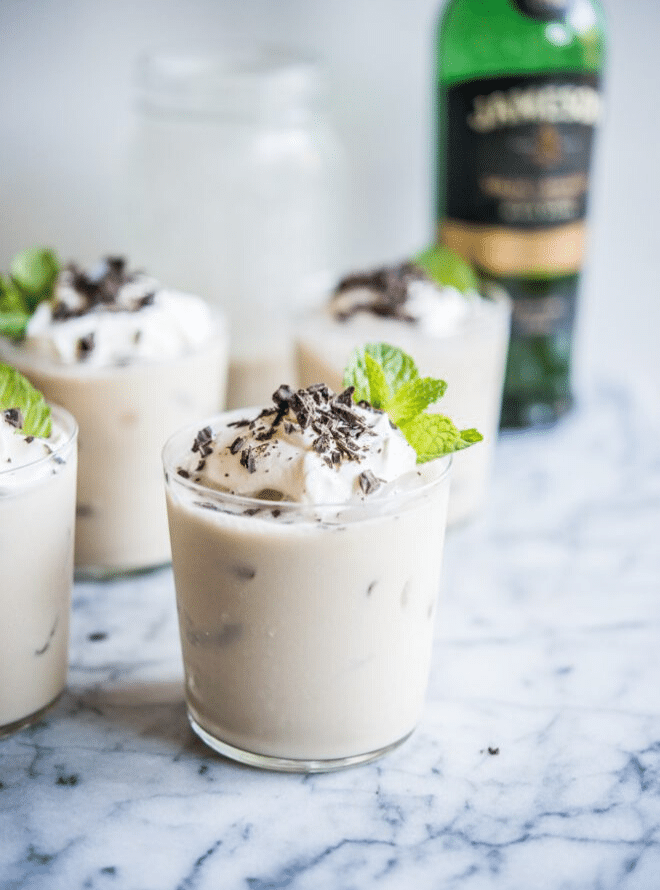 clear glasses filled with vegan baileys and topped with whipped cream, shaved chocolate, and mint leaves