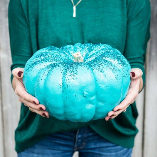 woman in a green shirt holding a teal pumpkin