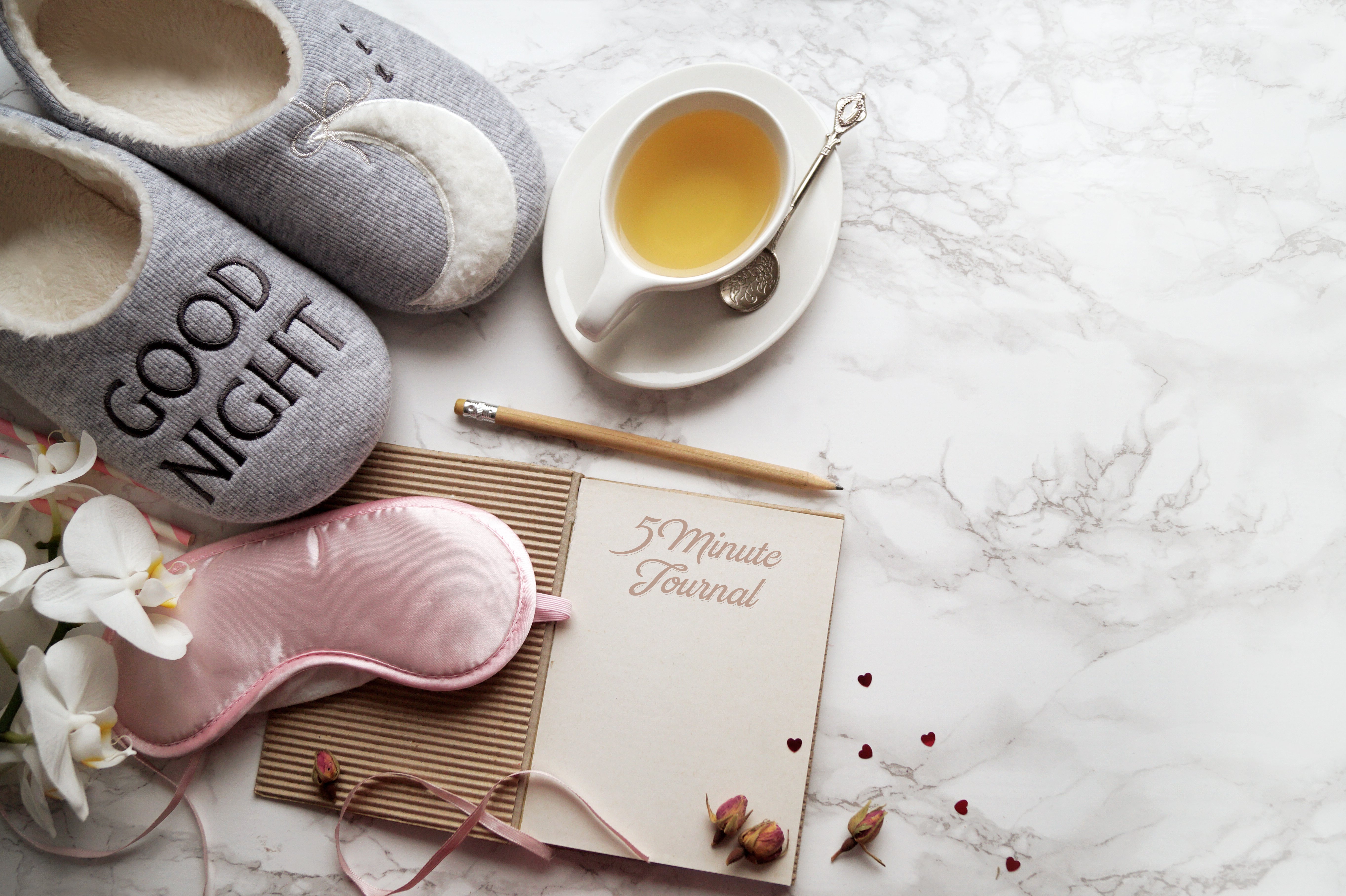 preparing your body for pregnancy - slippers, hot tea, eye mask, and journal on a marble surface