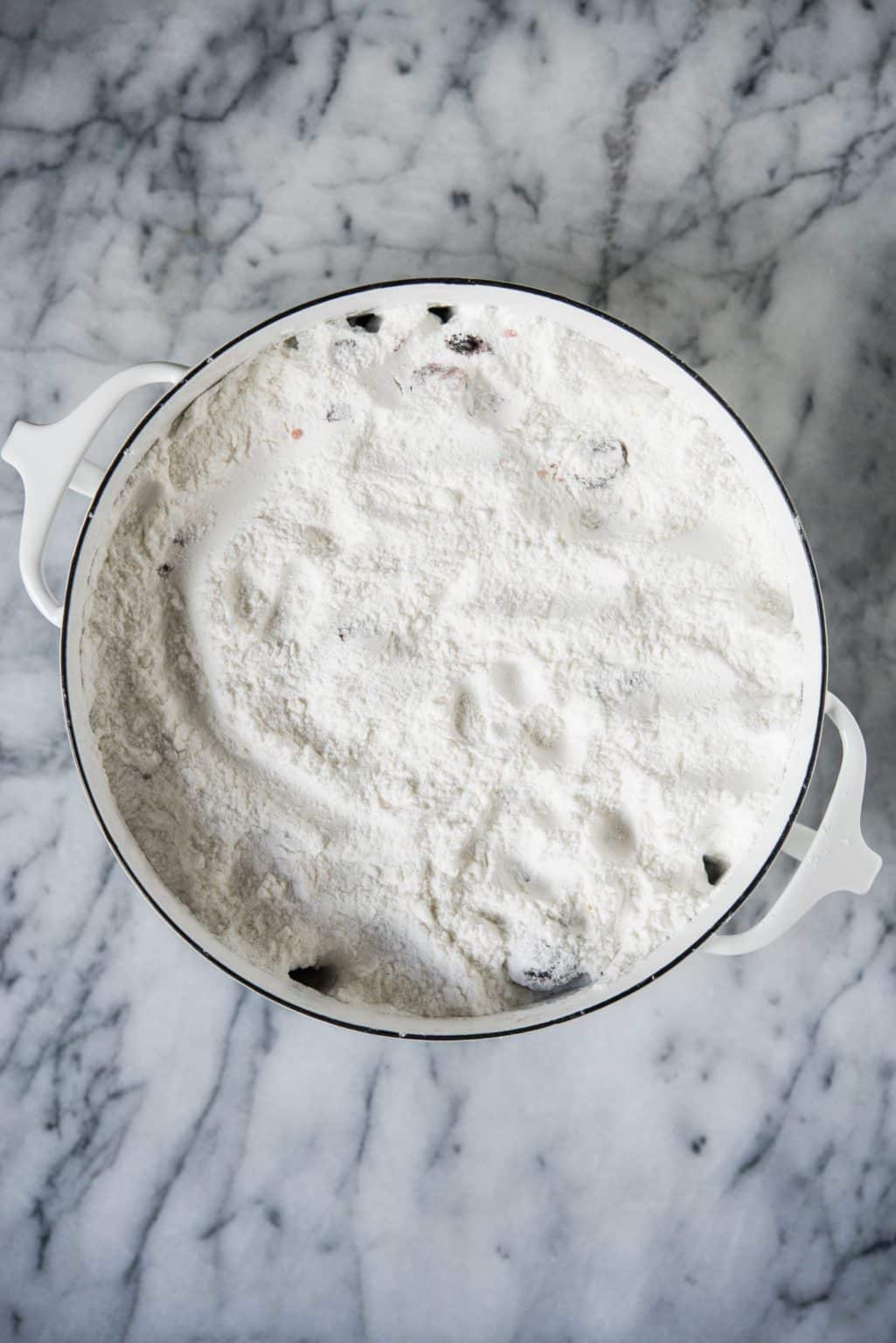 cherry dump cake batter in a round baking dish on a marble surface