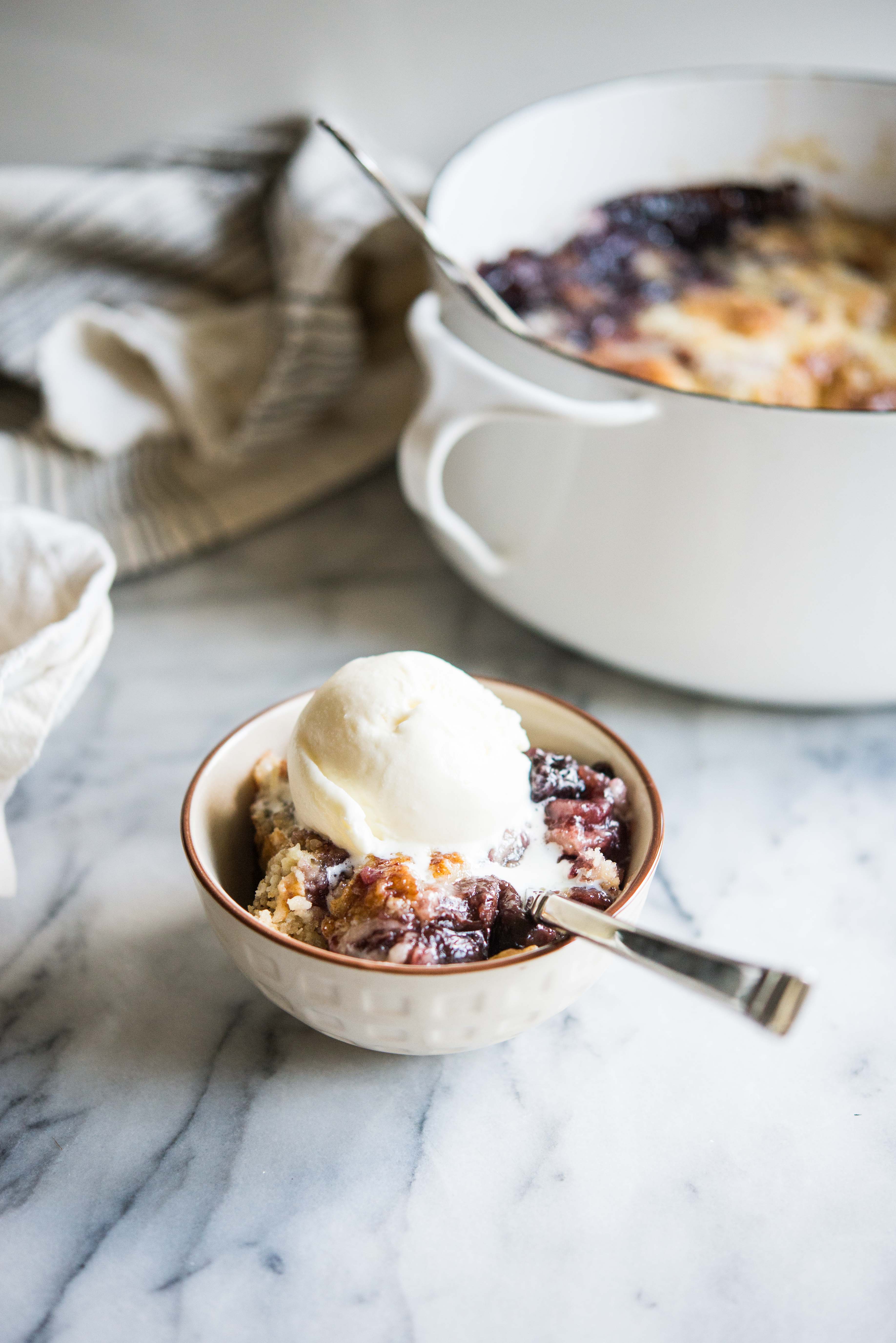 cherry dump cake in a white bowl with a scoop of ice cream on top