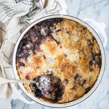 cherry dump cake in a round white baking dish with a scoop removed on a marble surface