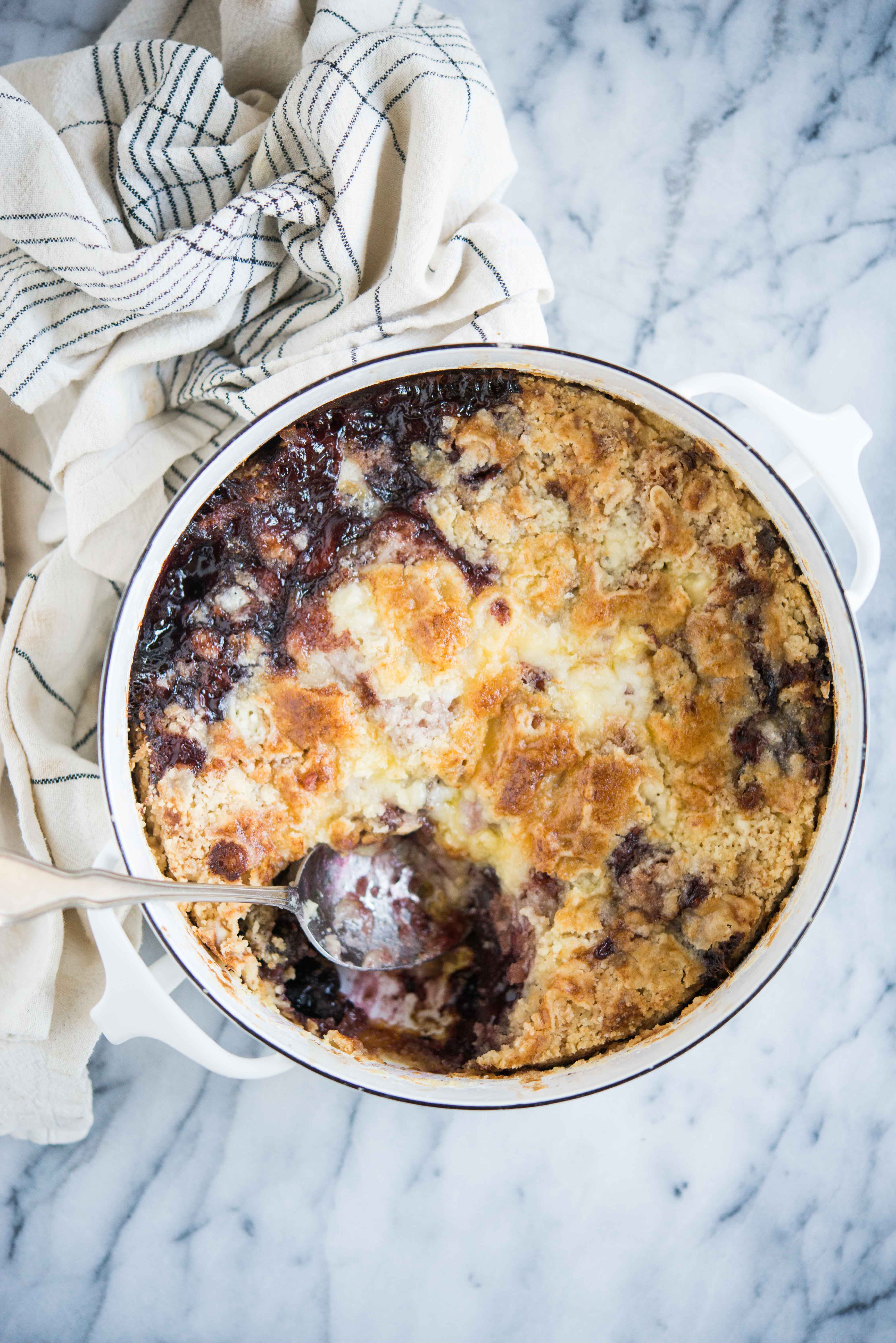 cherry dump cake in a round white baking dish with a scoop removed on a marble surface