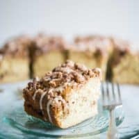 pastel de café con canela con glaseado rociado en la parte superior sobre un plato de vidrio con un tenedor sentado junto a él sobre una superficie de mármol