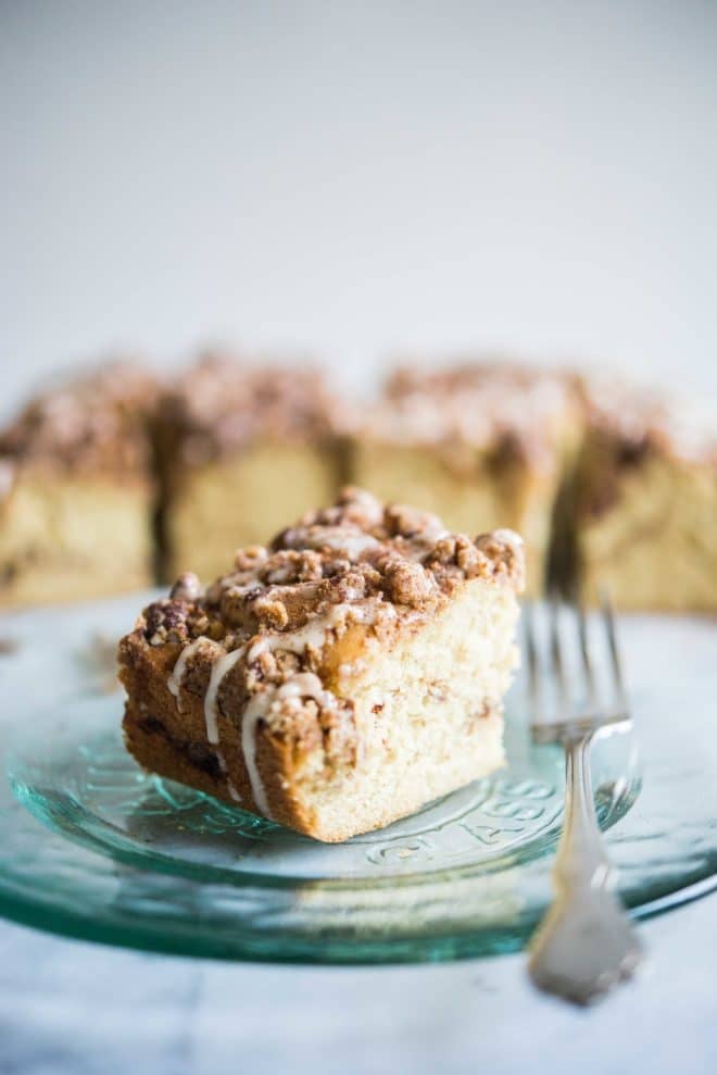 cinnamon coffee cake with icing drizzled on top on a glass plate with a fork sitting beside it on a marble surface