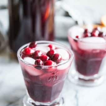 cranberry sangria in a glass with fresh cranberries and ice on a marble board