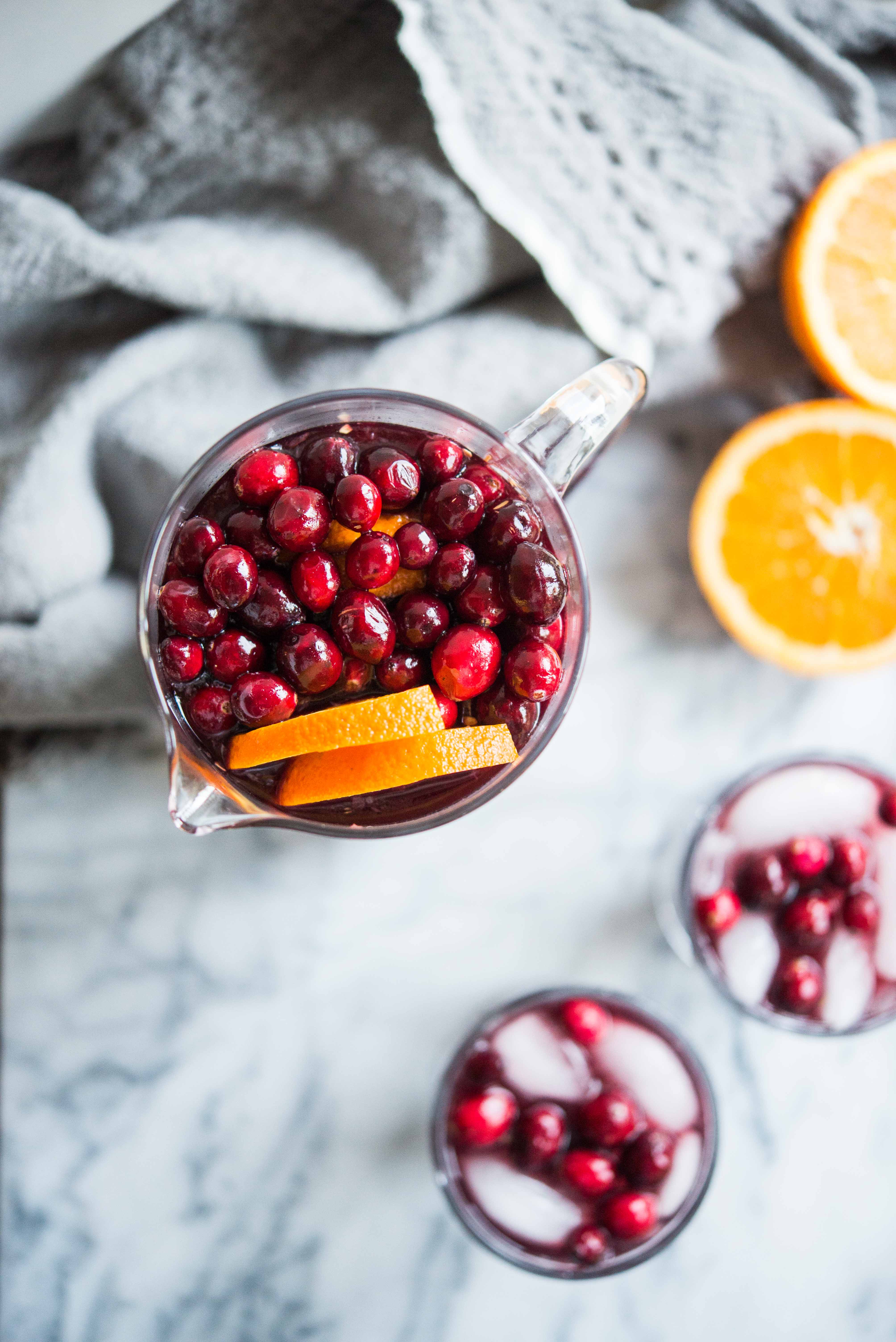 christmas cranberry sangria - overhead shot of Red sangria in a glass pitcher topped with oranges and cranberries next to two glasses filled with sangria on a marble board