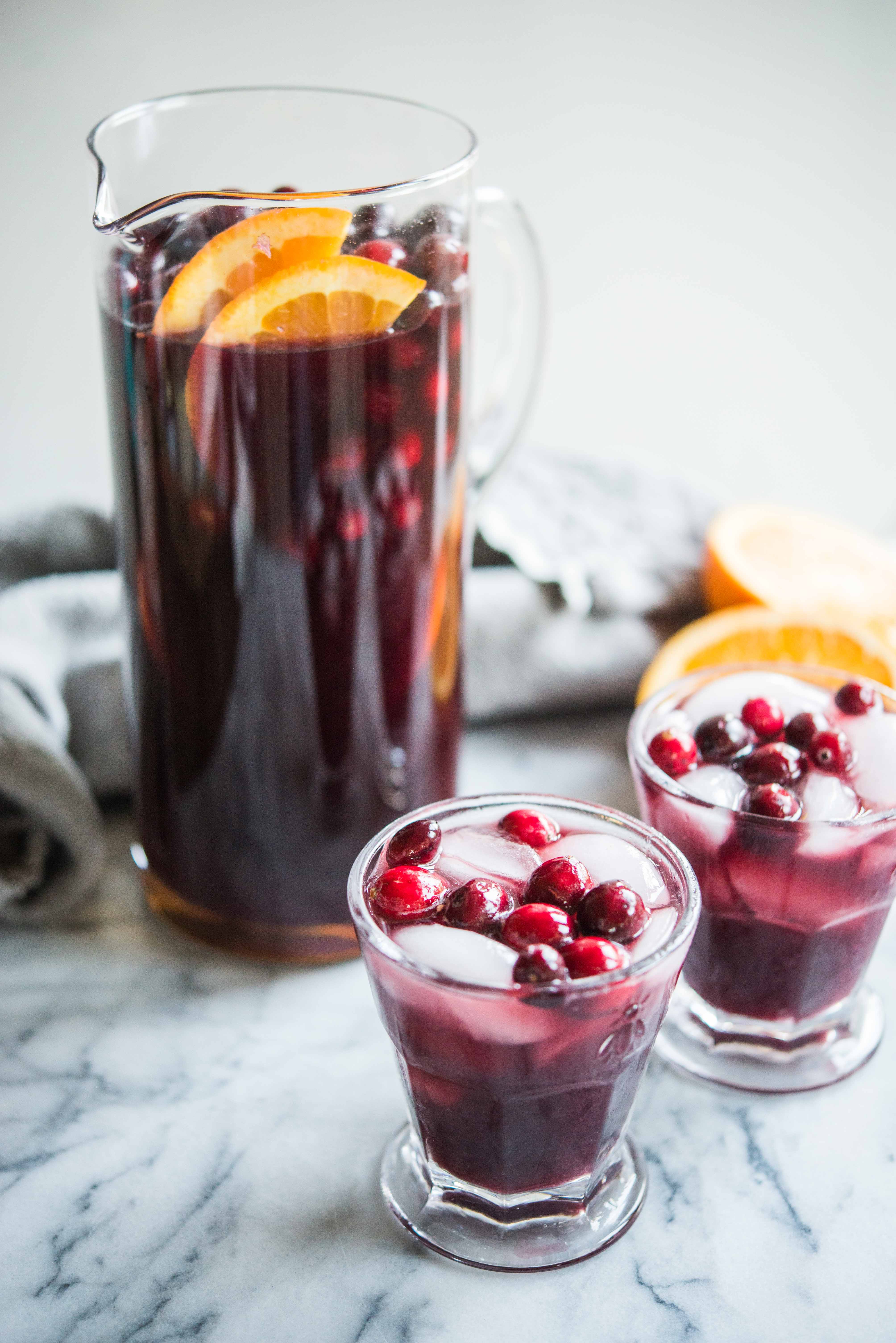 cranberry sangria - the perfect christmas sangria! Red sangria in a glass pitcher topped with oranges and cranberries next to two glasses filled with sangria on a marble board