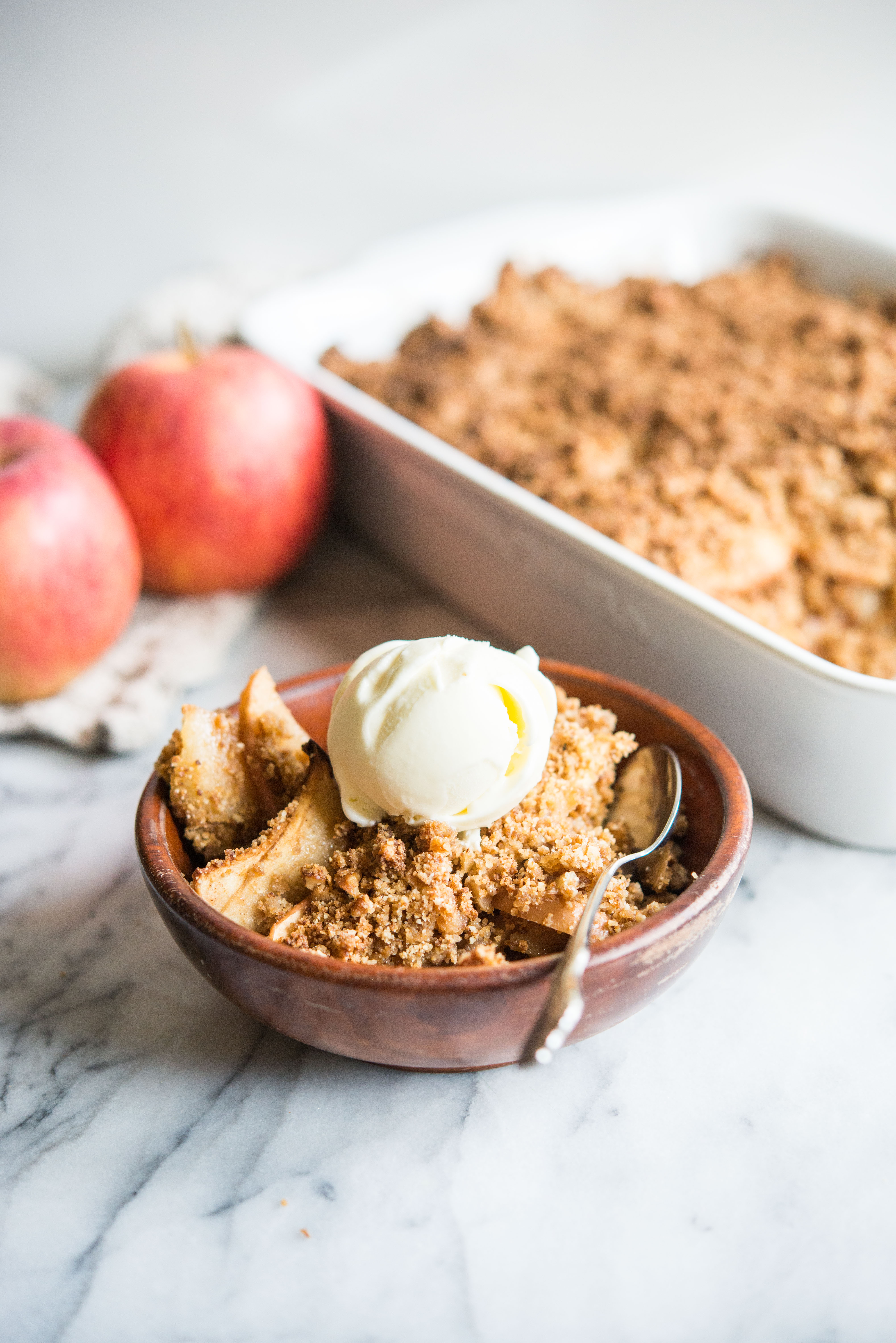 paleo apple crisp in a wooden bowl topped with a scoop of ice cream on a marble surface