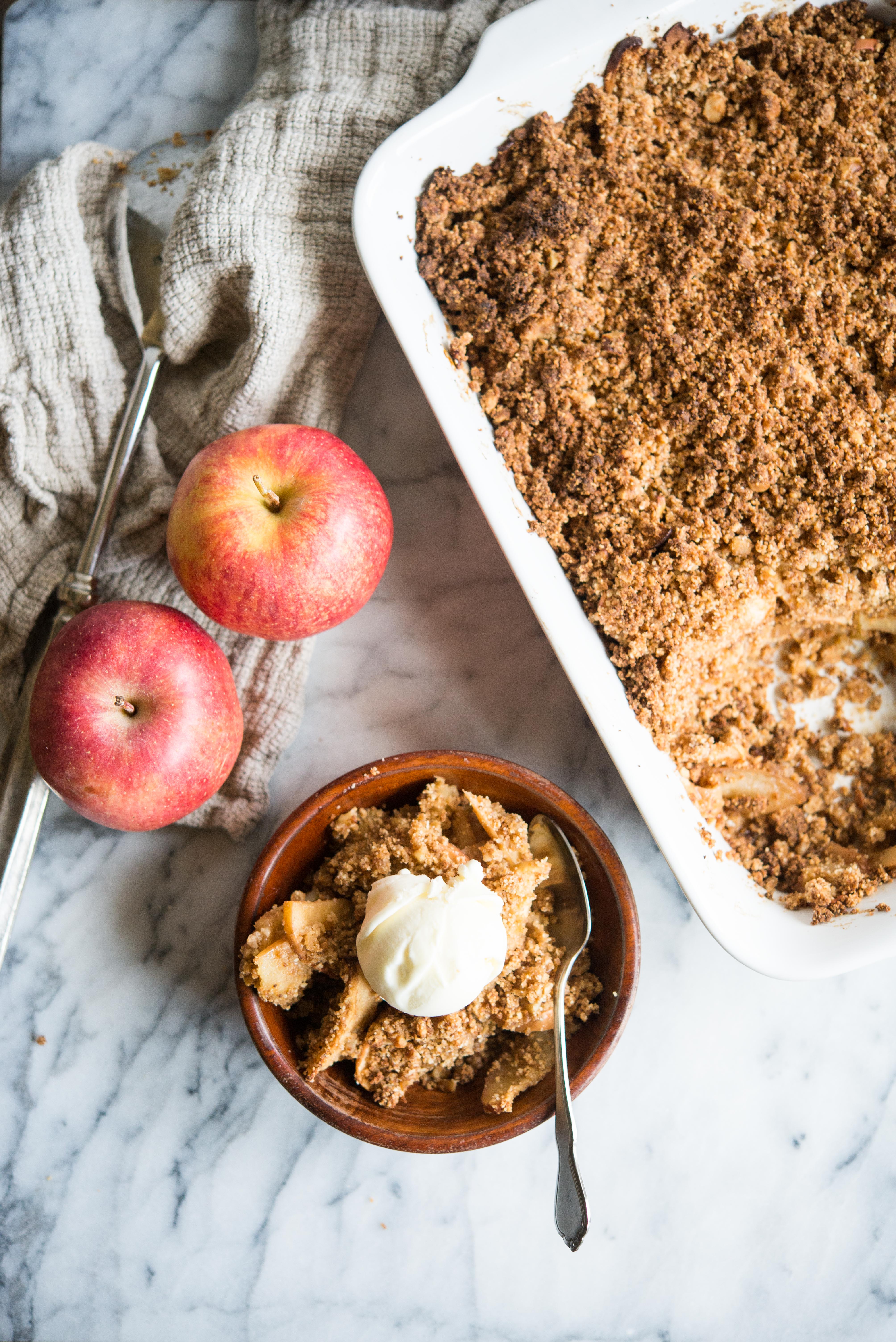 paleo apple crisp in a white rectangular dish with some spooned out into a wooden bowl and topped with a scoop of ice cream