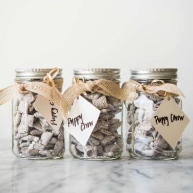 3 jars of puppy chow in glass jars with a brown ribbon wrapped around each and a gift tag attached
