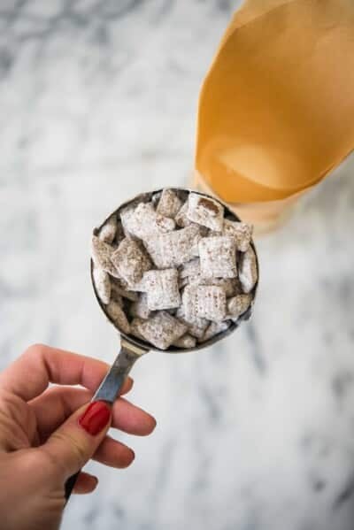 measuring cup full of puppy chow being poured into a parchment paper cone in a mason jar