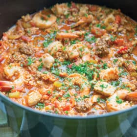 shrimp jambalaya with chicken and sausauge in a large green cast iron pot with chopped parsley on top