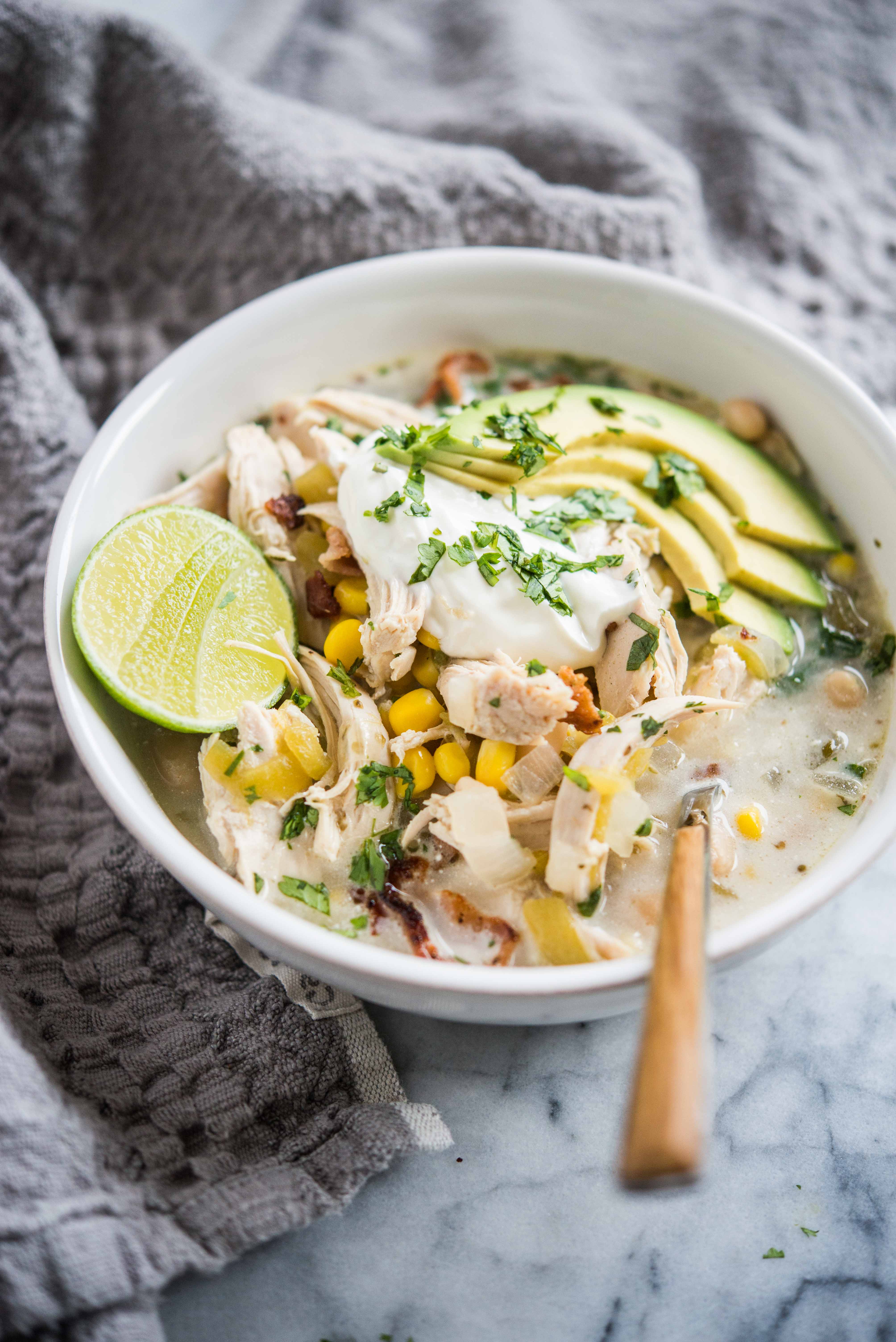 easy white chicken chili in a bowl topped with lime, sour cream, avocado, and cilantro on a marble surface with a grey towel beside it