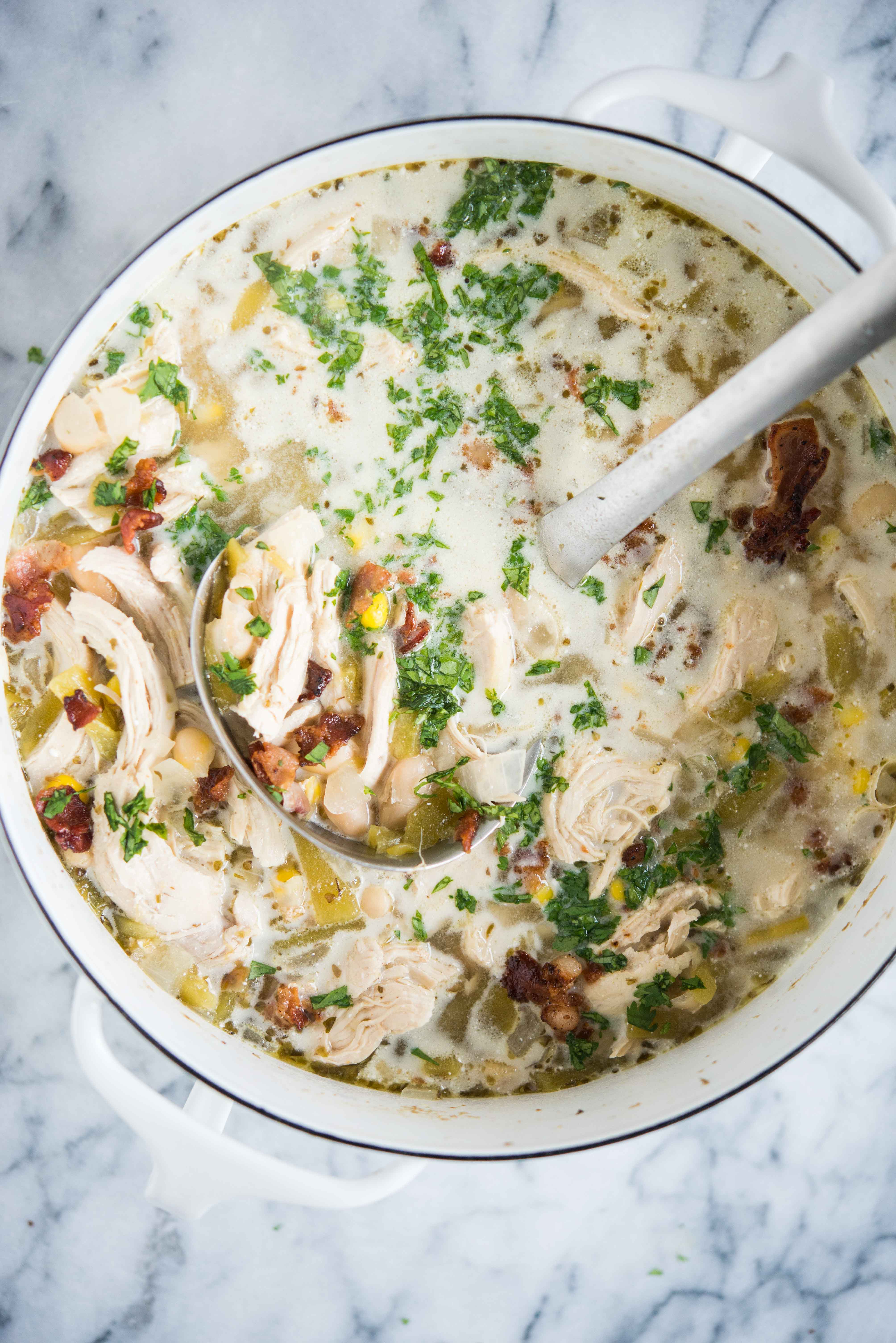 white chicken chili with chopped cilantro on top in a white pot on a marble surface