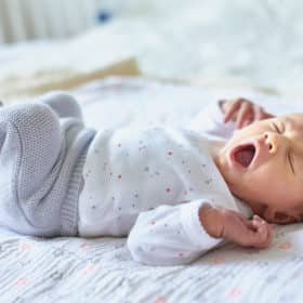 Adorable newborn baby girl sleeping and yawning in bed at home - sleep training methods