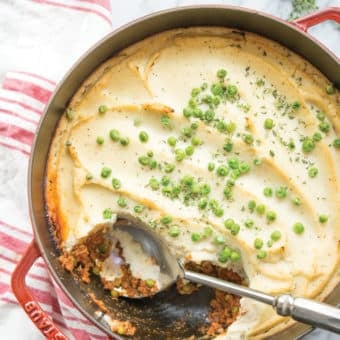 cottage pie with cauliflower mash in a red cast iron pot on a white background with a red and white striped towel lying next to it