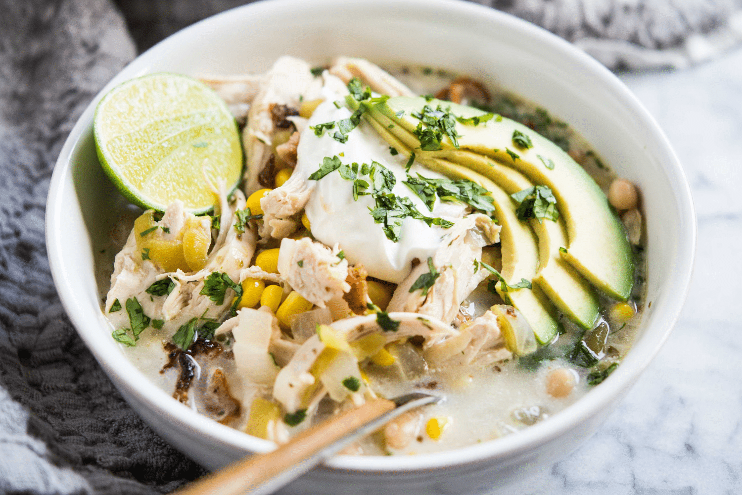 easy white chicken chili in a bowl topped with lime, sour cream, avocado, and cilantro on a marble surface with a grey towel beside it