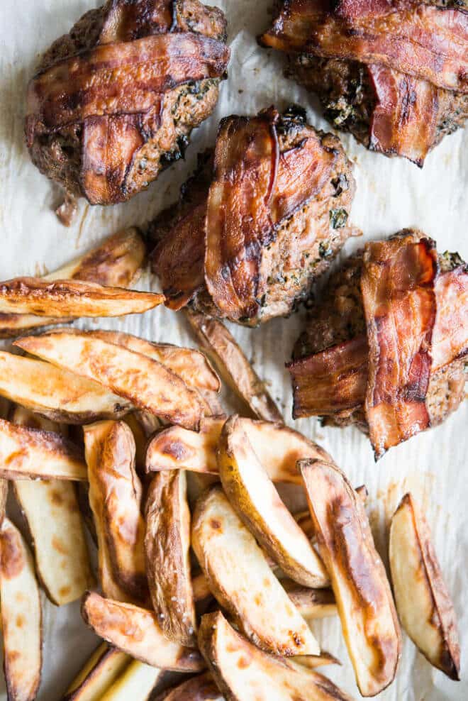 mini meatloaf topped with bacon on parchment paper beside roasted fries