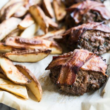 mini meatloaf topped with bacon on parchment paper beside roasted fries