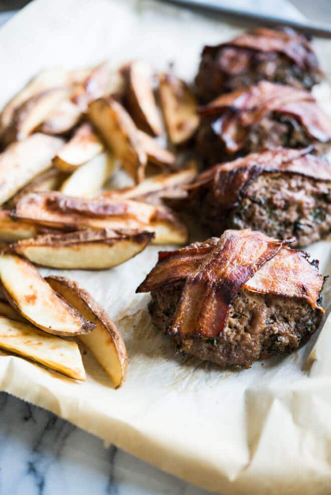 mini meatloaf topped with bacon on parchment paper beside roasted fries