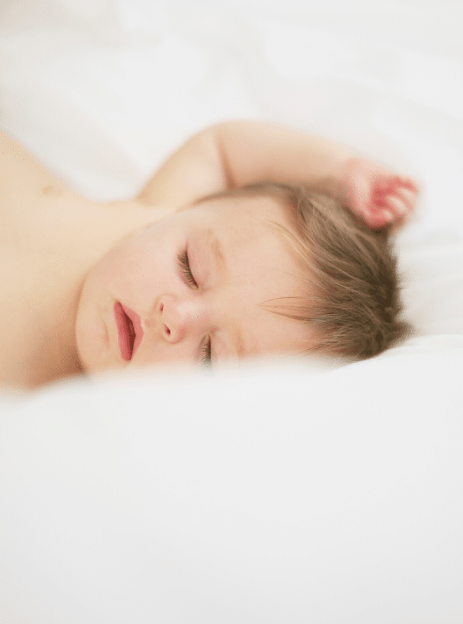 baby boy asleep on white sheets with his arm over his head - baby sleep