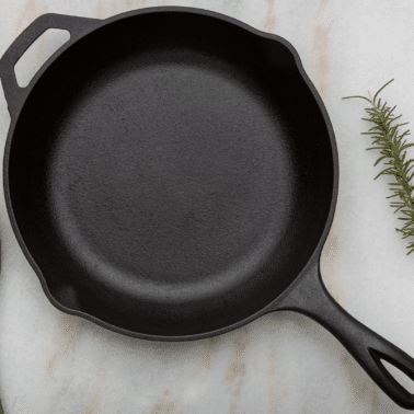 cast iron pan on marble surface with rosemary and wooden spoon