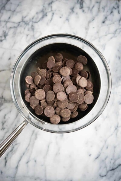 chocolate chips in a glass bowl over a stainless steel pot on a marble surface