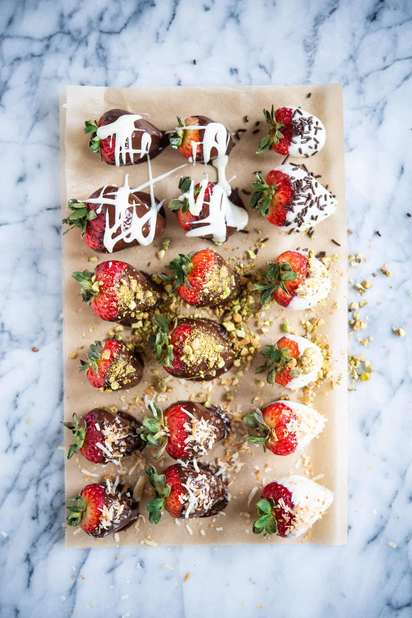 white and dark chocolate covered strawberries with different toppings on parchment paper on a marble surface